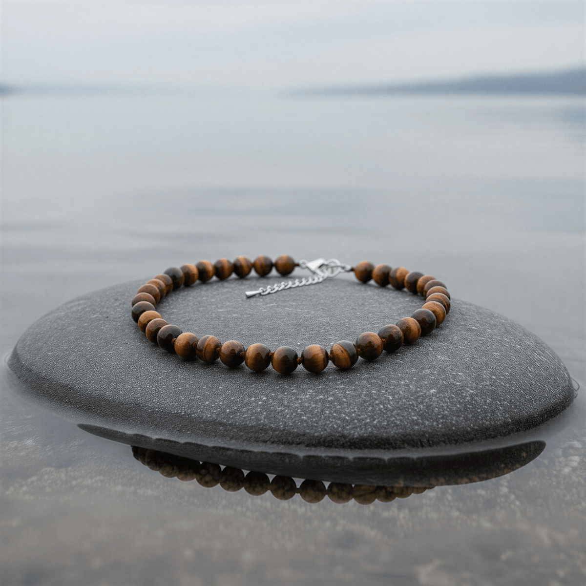 Bruine handgeknoopte edelstenen ketting met tijgeroog en sterling zilver (925) liggend op steen in water zijaanzicht | Tiger Eye Ball