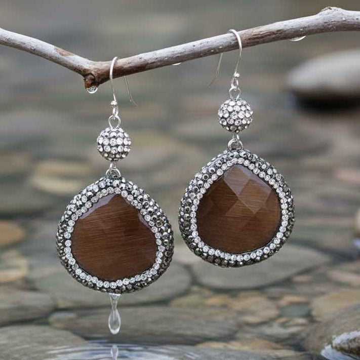 Bruine edelstenen oorbellen met kattenoog, stras steentjes en sterling zilver (925) hangend aan takje boven water | Bright Brown Cat’s Eye