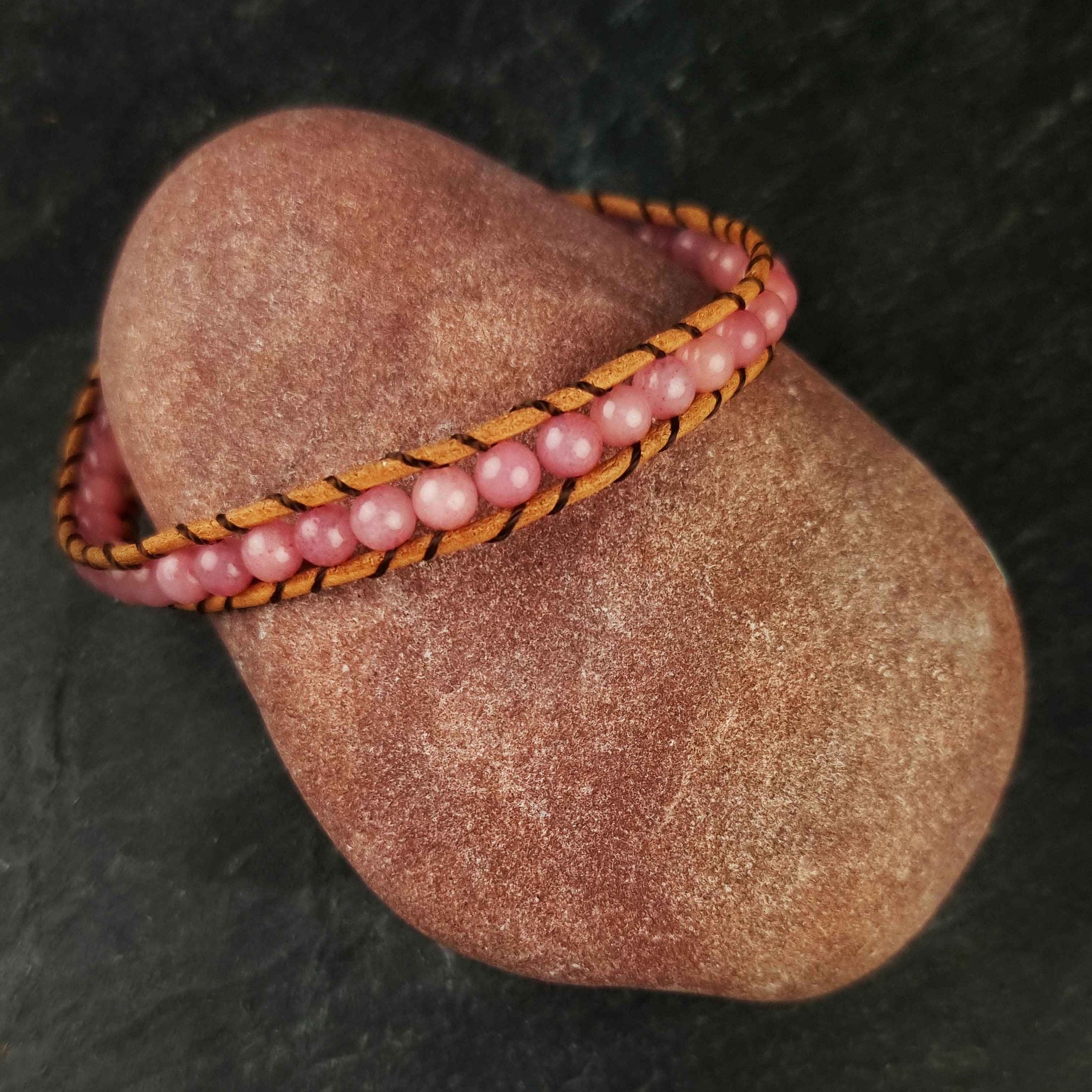 Roze edelstenen armband met rozenkwarts en bruin leer liggend op rode steen | Wrap Little Rose Quartz