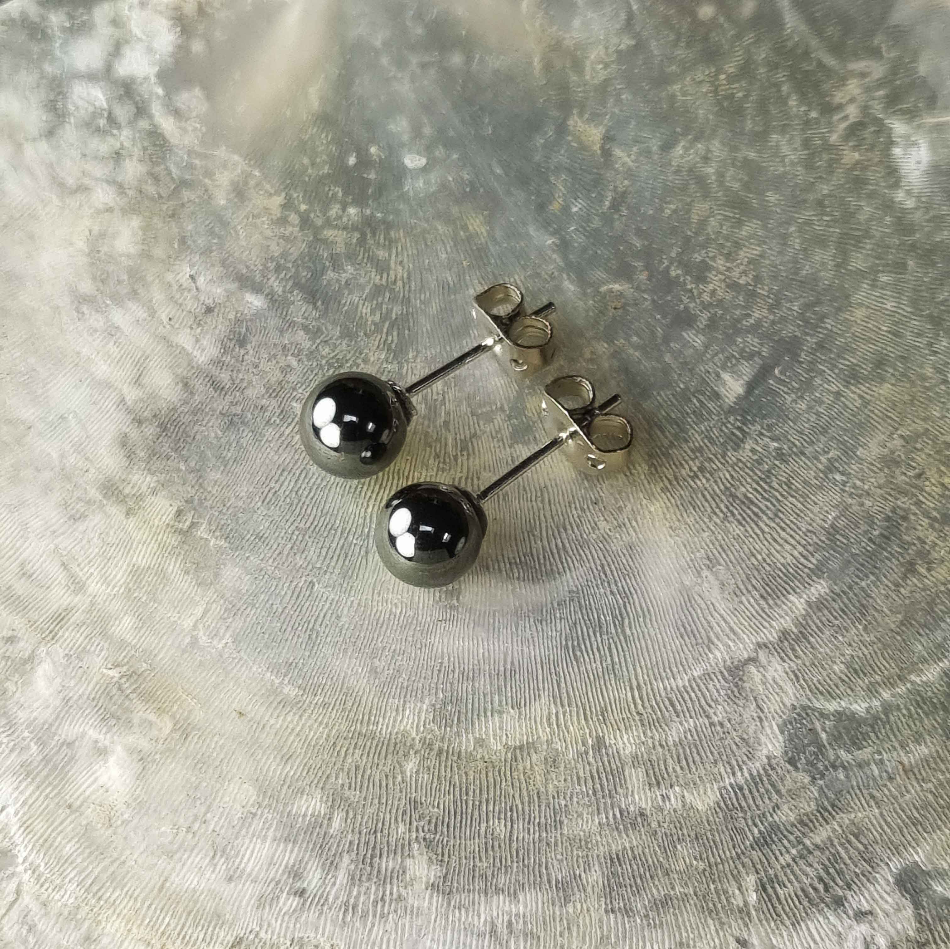 Zwarte edelstenen oorbellen met hematiet stenen, zwarte hematiet oorknopjes 6 mm liggend op witte schelp bovenaanzicht | Hematite Stud 6 mm