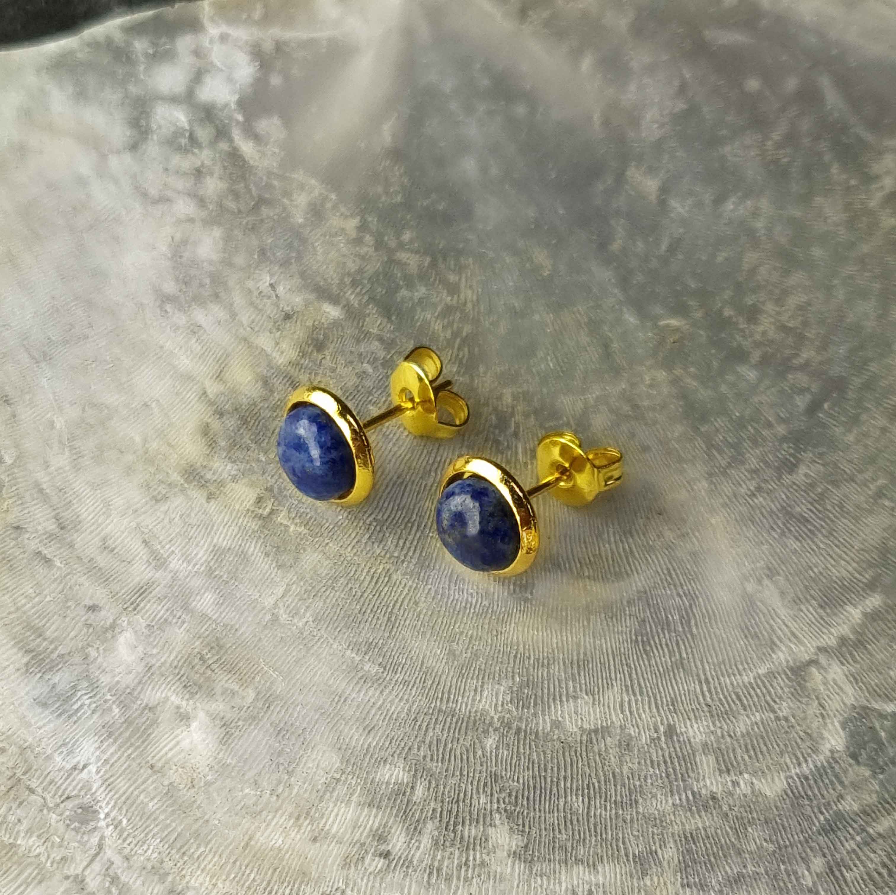 Blauwe edelstenen oorbellen met lapis lazuli, lapis lazuli oorknopjes liggend op witte schelp