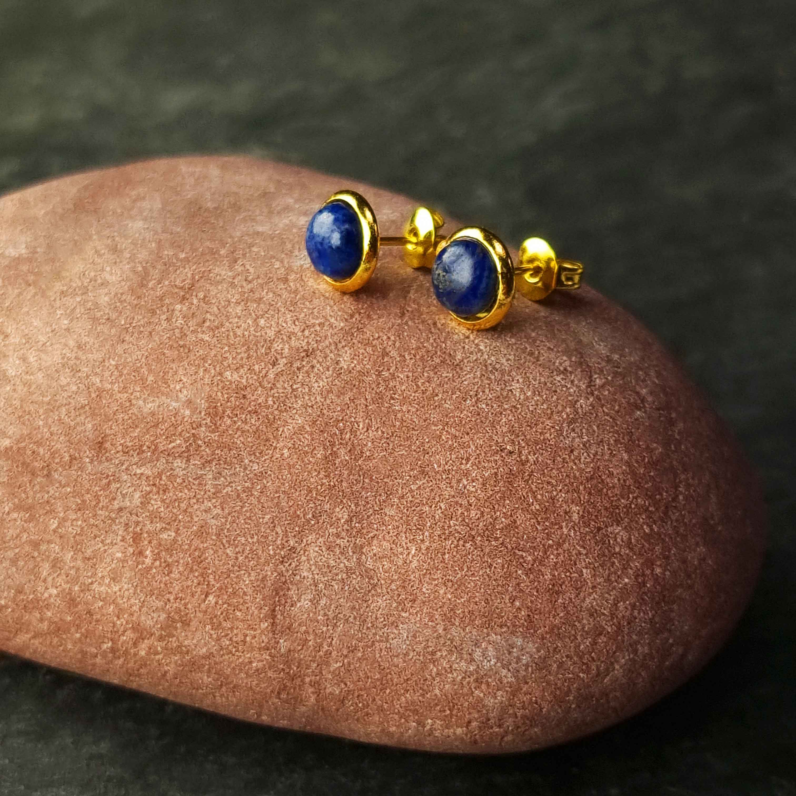 Blauwe edelstenen oorbellen met lapis lazuli, lapis lazuli oorknopjes liggend op rode steen, zijaanzicht