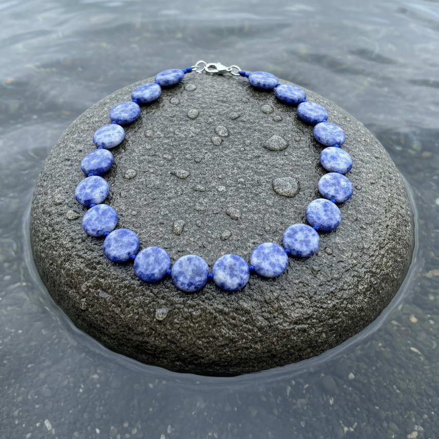 Blauwe handgeknoopte edelstenen ketting met blue spot jaspis stenen liggend op steen in water | Blue Spot Coin