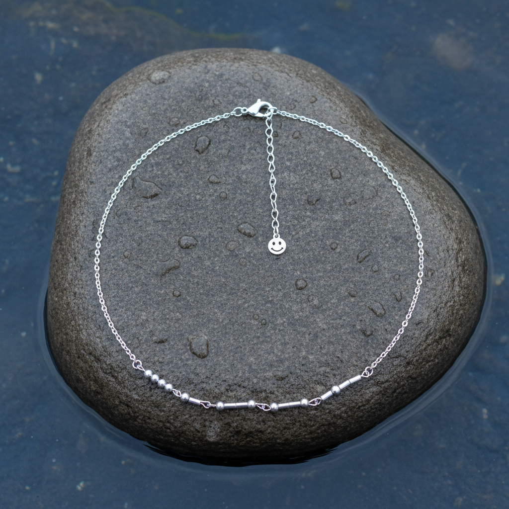 Zilveren edelstenen ketting met zilver edelstaal en hematiet stenen die het woord HAPPY in morse code weer geeft liggend op steen in water | Morse Code Happy Silver Hematite