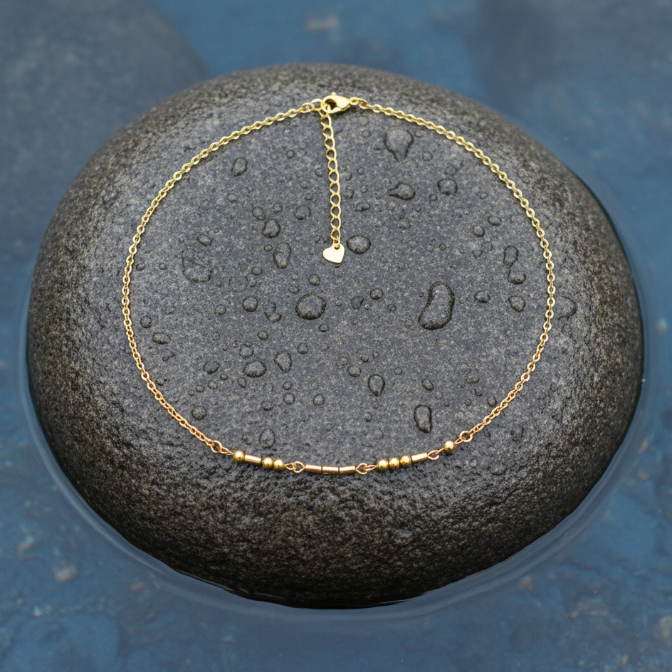 Gouden edelstenen ketting met goud edelstaal en hematiet stenen die het woord LOVE in morse code weer geeft liggend op steen in water | Morse Code Love Gold