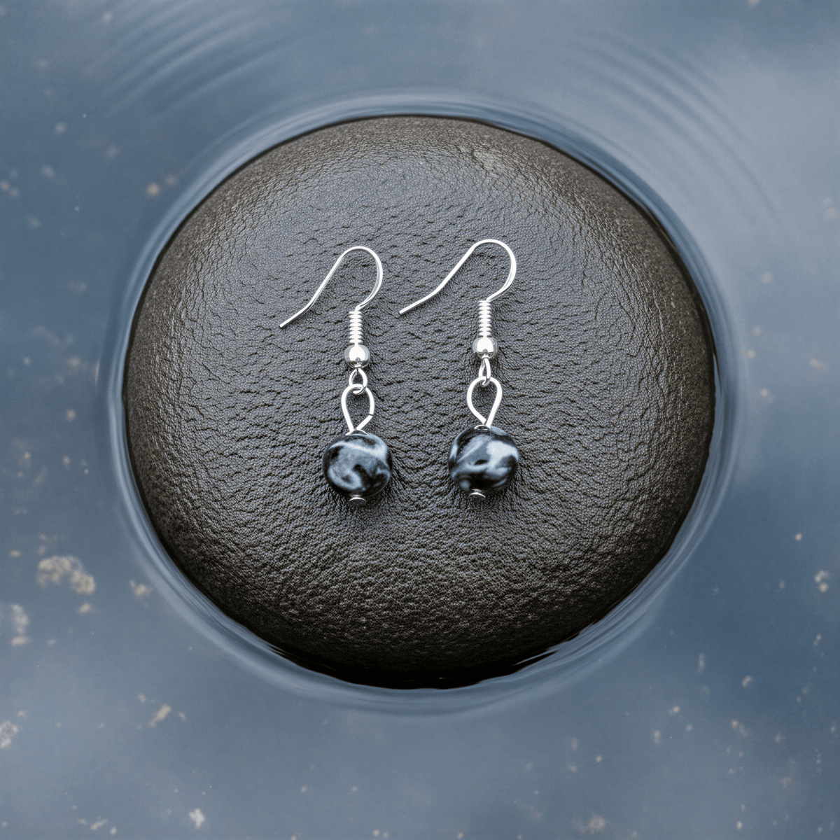 Edelstenen oorbellen met zwarte labradoriet en sterling zilver (925) liggend op steen | Dangling Black Labradorite