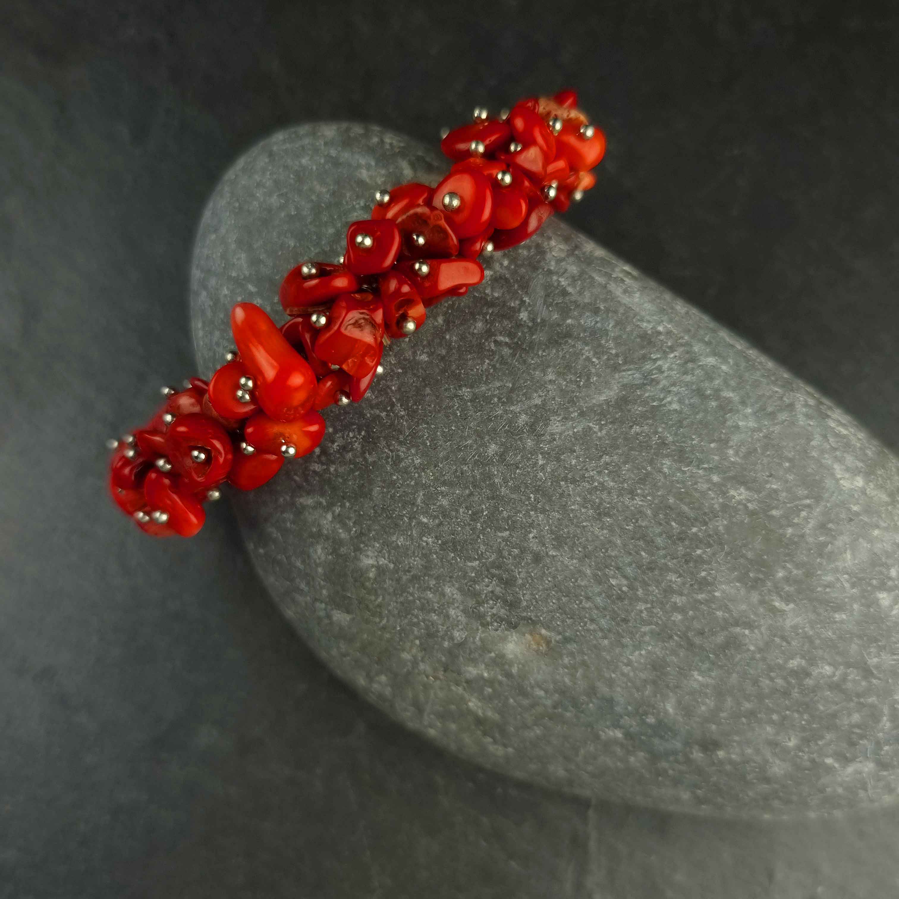 Dik rood koralen armband met stukjes koraal liggend tegen kei | Coral Chip