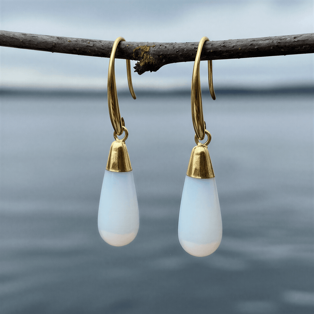 Licht blauwe edelsten oorbellen met opaal hangend aan takje boven water | Long Gold Dip Sea Opal