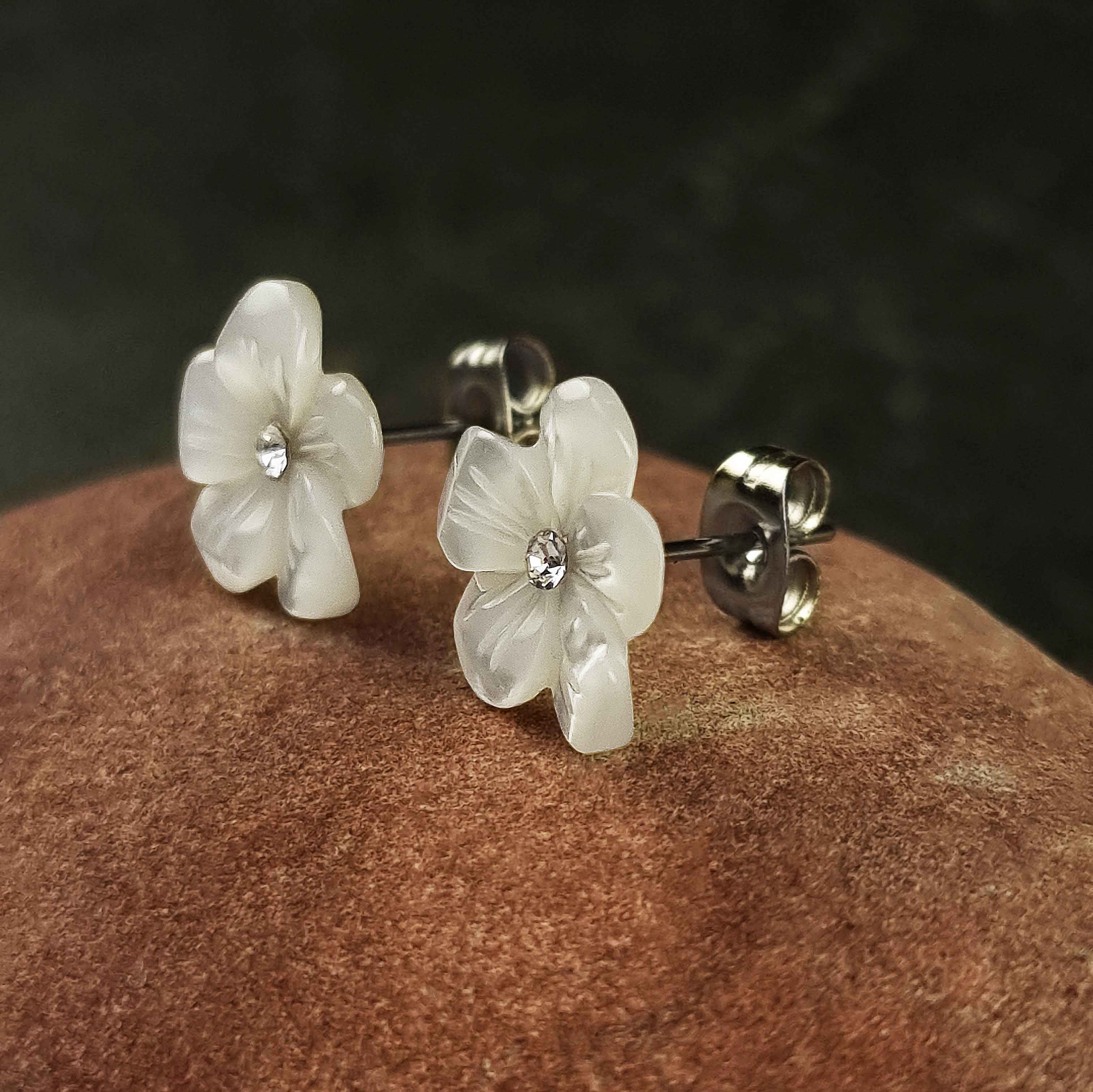 Witte parelmoeren oorknopjes met bloem en stras steentje liggend op rode steen, zijaanzicht | Big Flower Bling