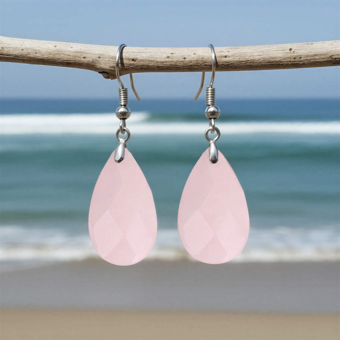 Roze edelstenen oorbellen met rozenkwarts en sterling zilver 925 hangend aan takje met achtergrond zee | Facet Rosé Quartz