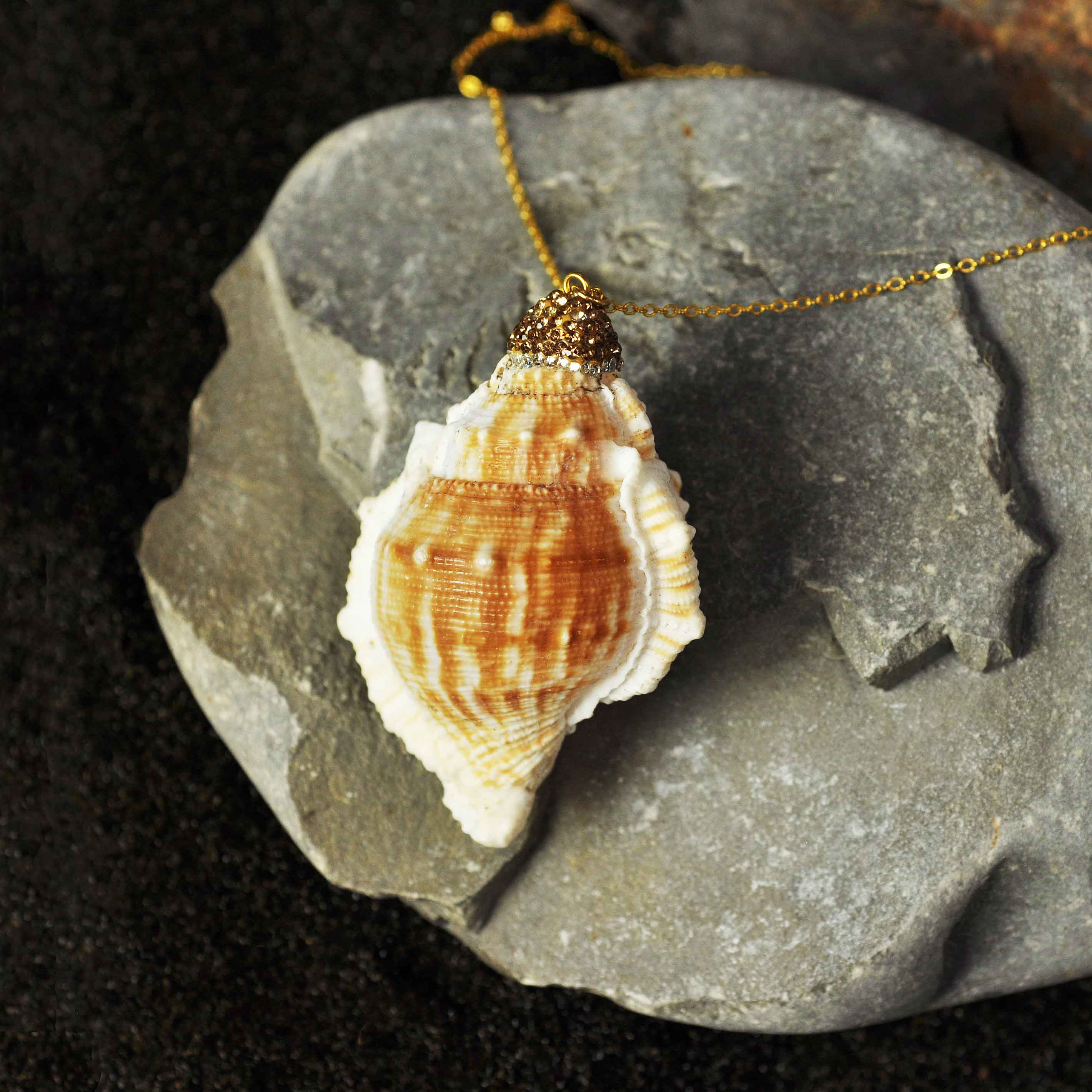 Schelpenketting met goud edelstaal en glitters liggend op grijze steen | Schelpen ketting Bright Golden Spiral Shell