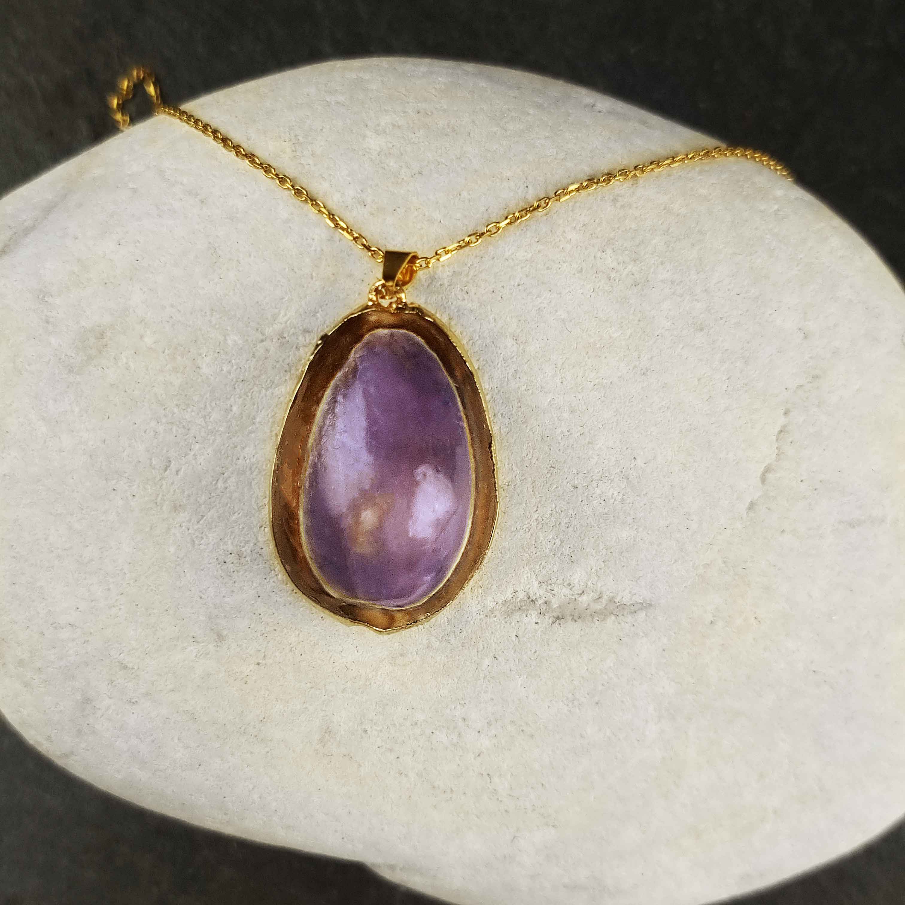 Paarse schelpenketting met schelpen hanger aan goud edelstalen ketting liggend op witte steen | Shell Cowrie Purple