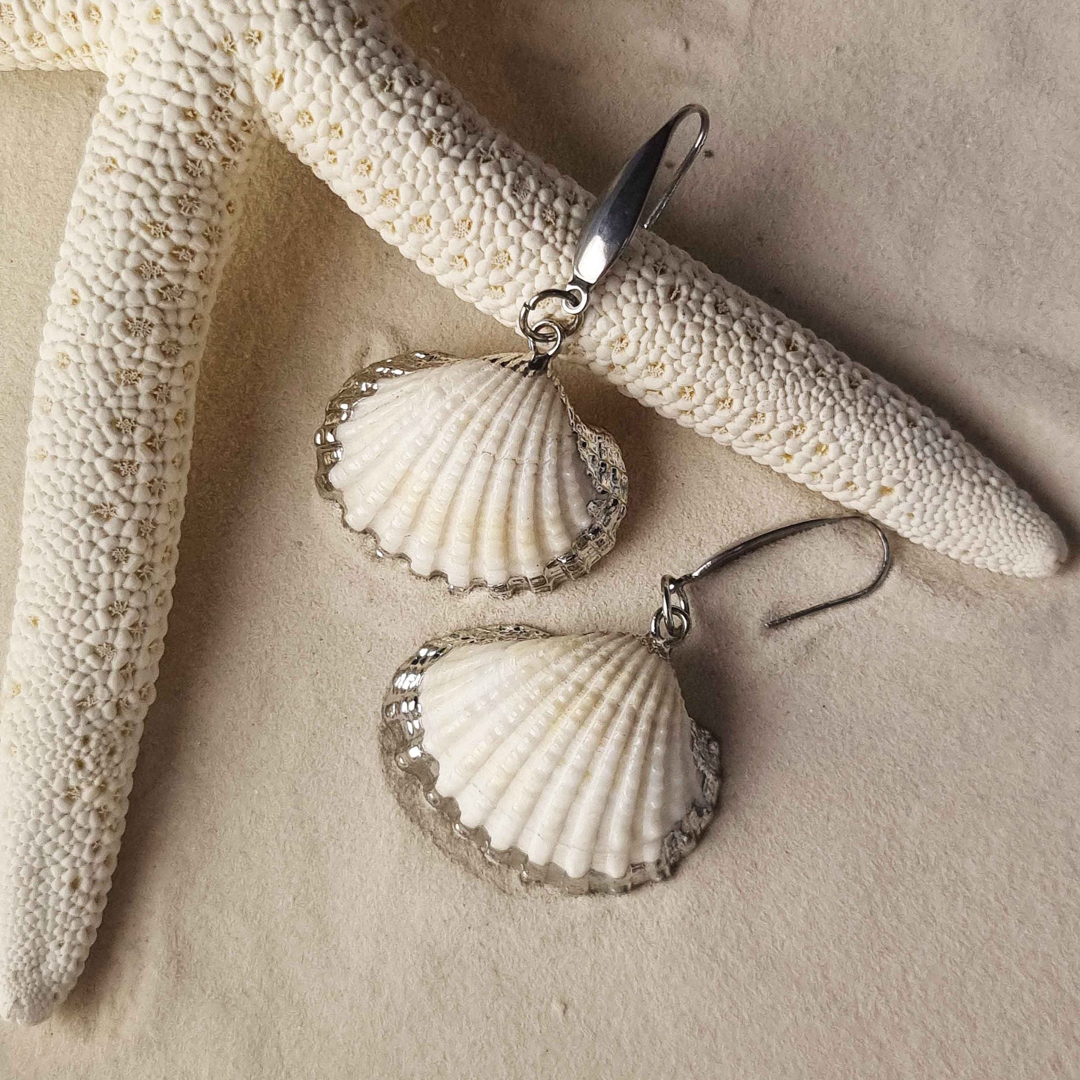 Witte schelp oorbellen met zilver edelstaal liggend op zand | White Cockel Shell Silver