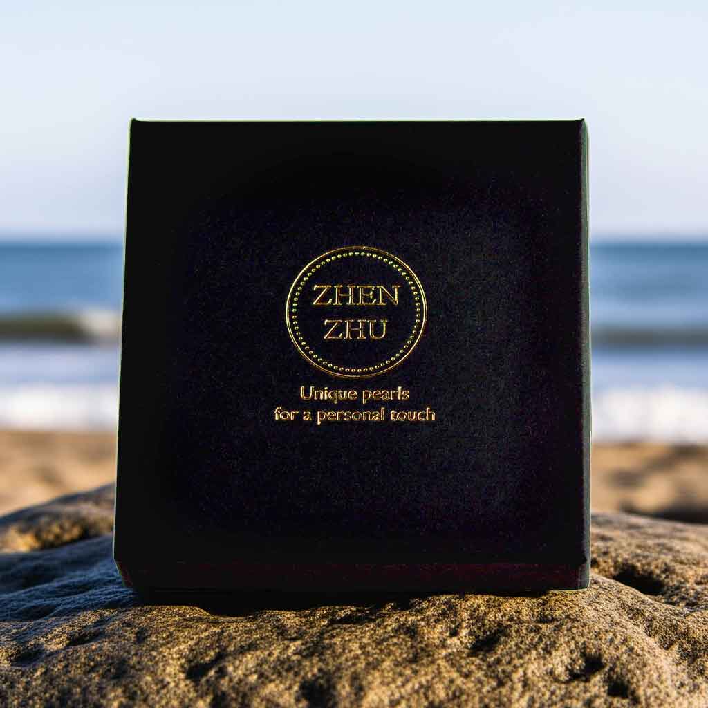 Zwart luxe sieraden doosje met gouden logo Zhen Zhu op rots bij strand