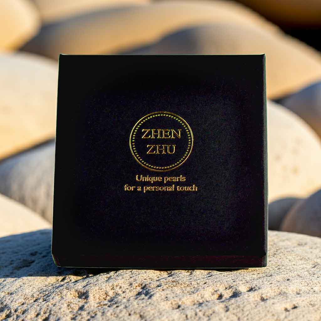 Zwart vierkant sieraden doosje met gouden logo Zhen Zhu op bruine stenen