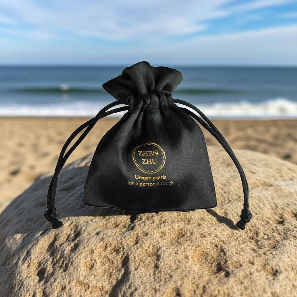 Zwart satijnen sieraden zakje met gouden logo Zhen Zhu liggend op steen