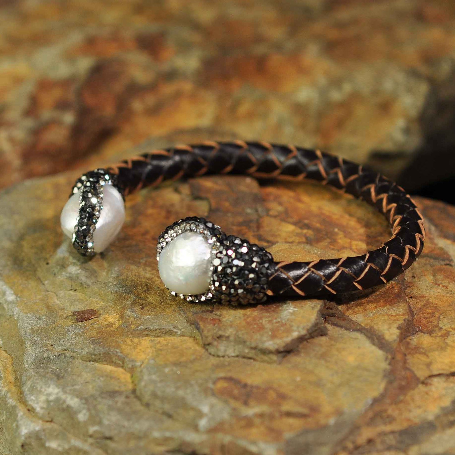 Wit zoetwater parel armband met stras steentjes en bruin gevlochten leer liggend op oranje steen| Bright Pearl Brown Leather Bangle