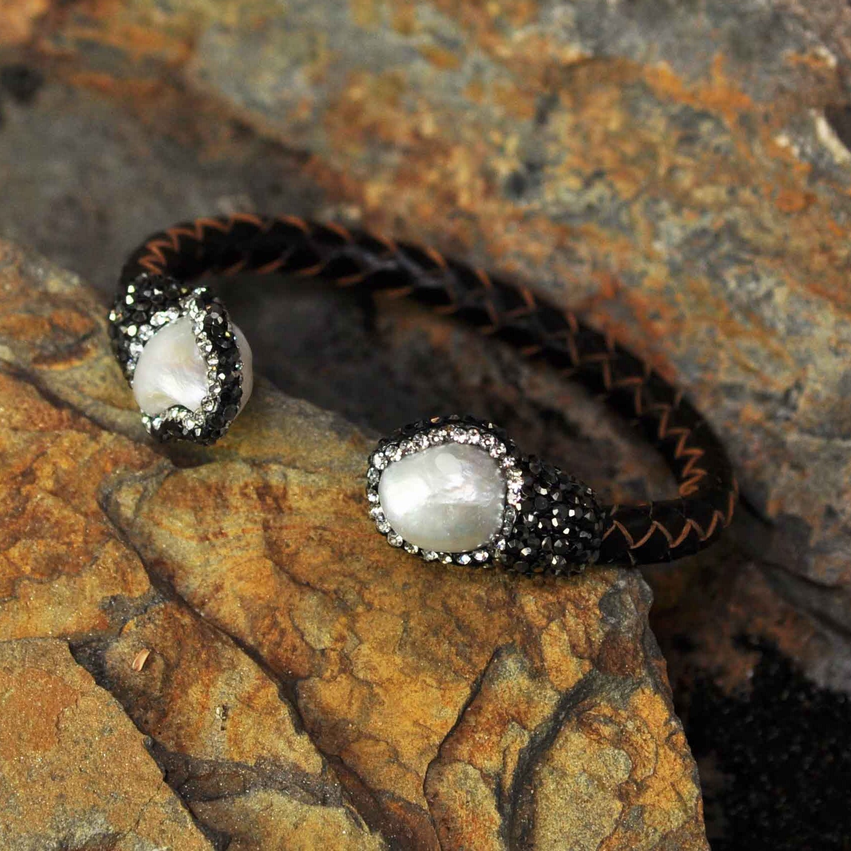 Wit zoetwater parel armband met stras steentjes en bruin gevlochten leer liggend tegen oranje steen| Bright Pearl Brown Leather Bangle