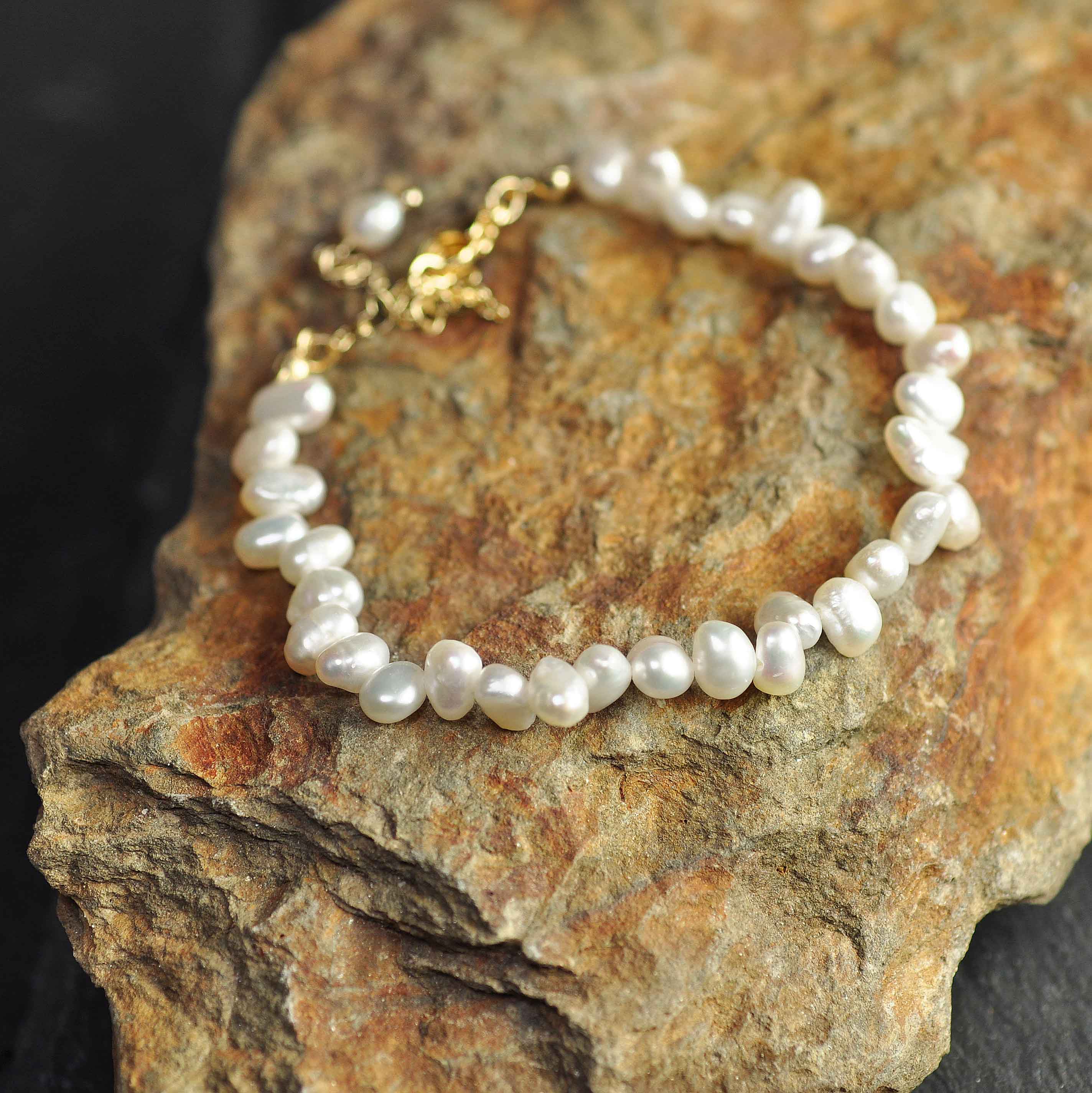 Wit zoetwater parel armband met goud edelstalen slotje en verlengketting liggend op oranje steen | Adalyn