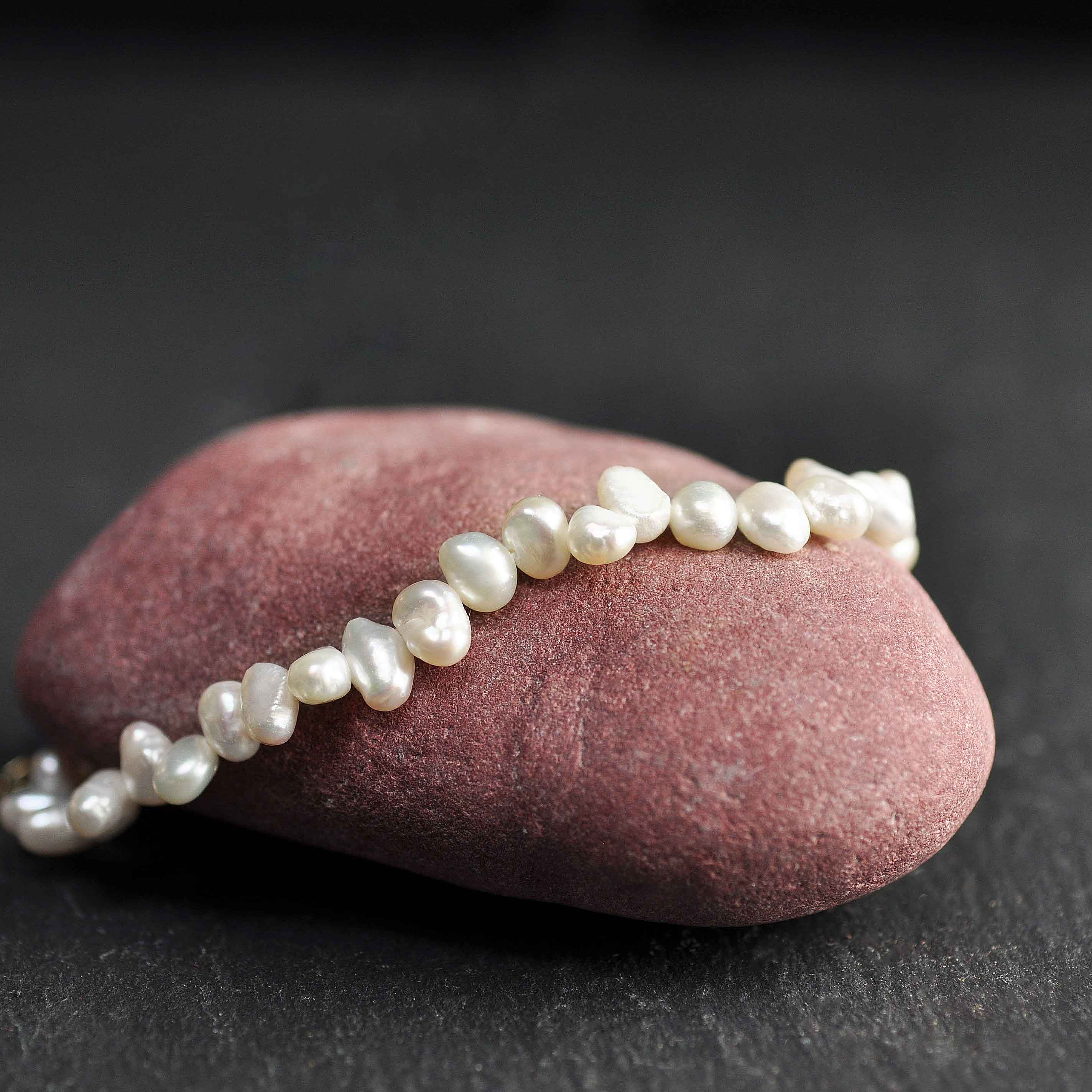 Wit zoetwater parel armband met goud edelstalen slotje en verlengketting liggend op rode steen | Adalyn