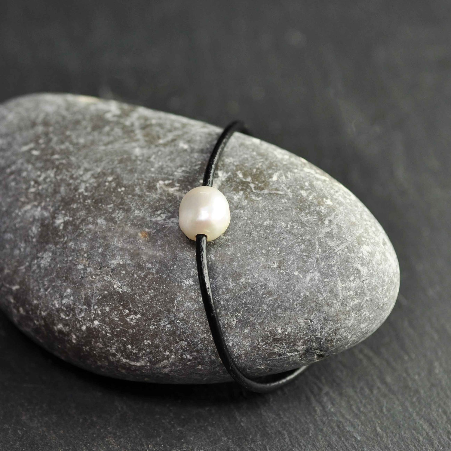 Wit zoetwater parel armband met zwart leer en magneetslot liggend op rots| Baliene