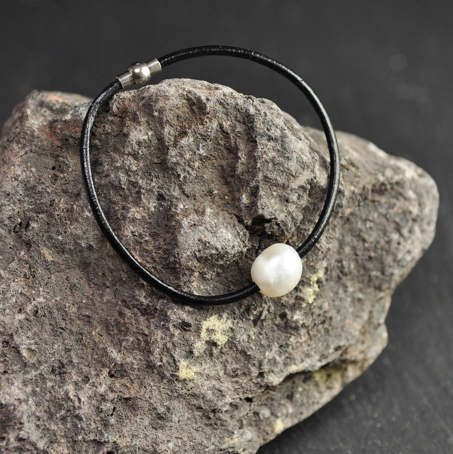 Wit zoetwater parel armband met zwart leer en magneetslot liggend op rots| Baliene