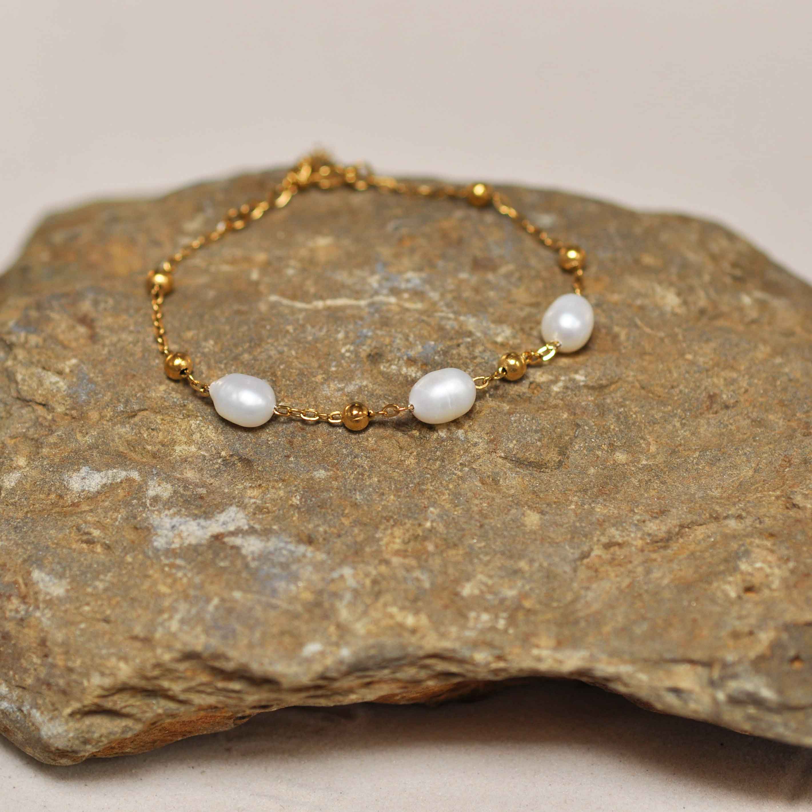 Wit zoetwater parel armband met goud edelstaal liggend op steen | Parel armband Eline Goud