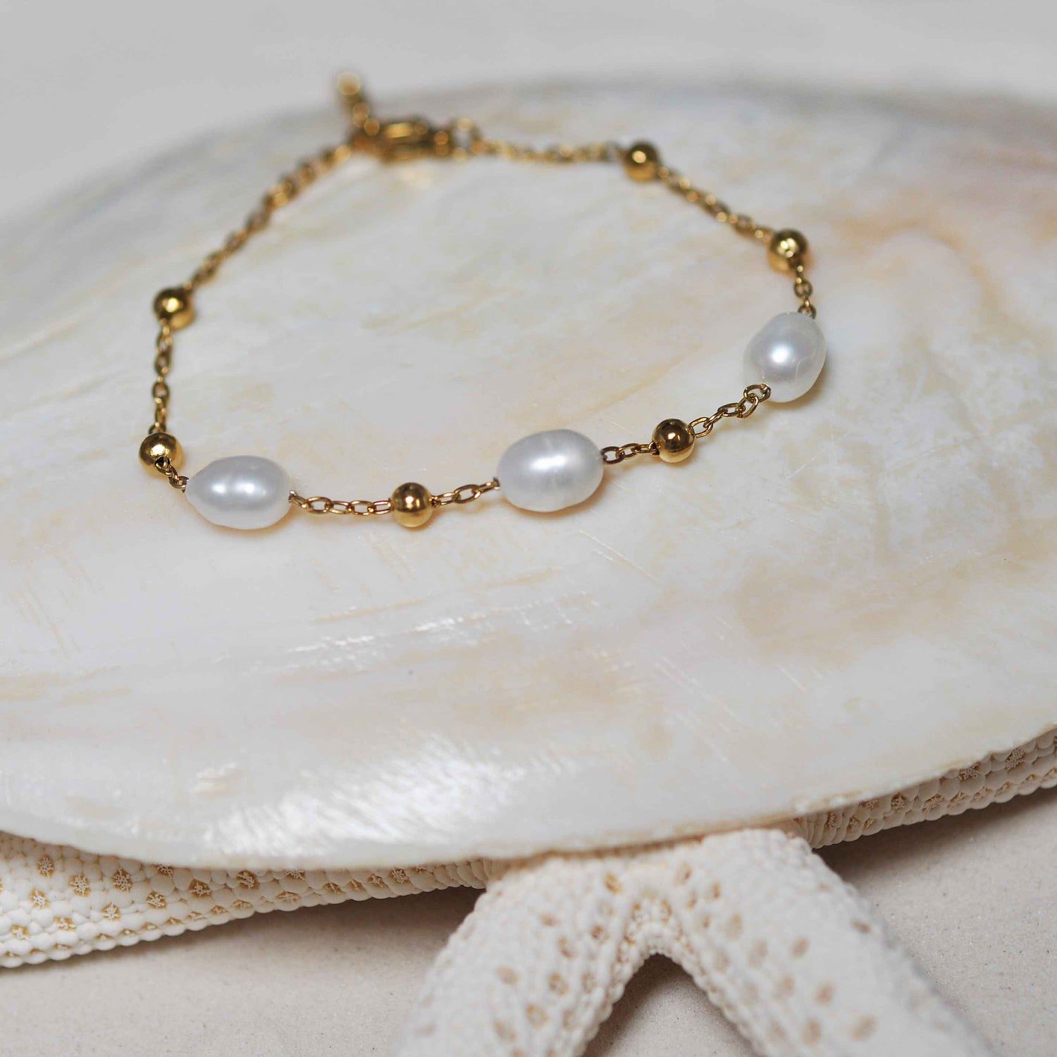 Wit zoetwater parel armband met goud edelstaal liggend op witte schelp | Parel armband Eline Goud