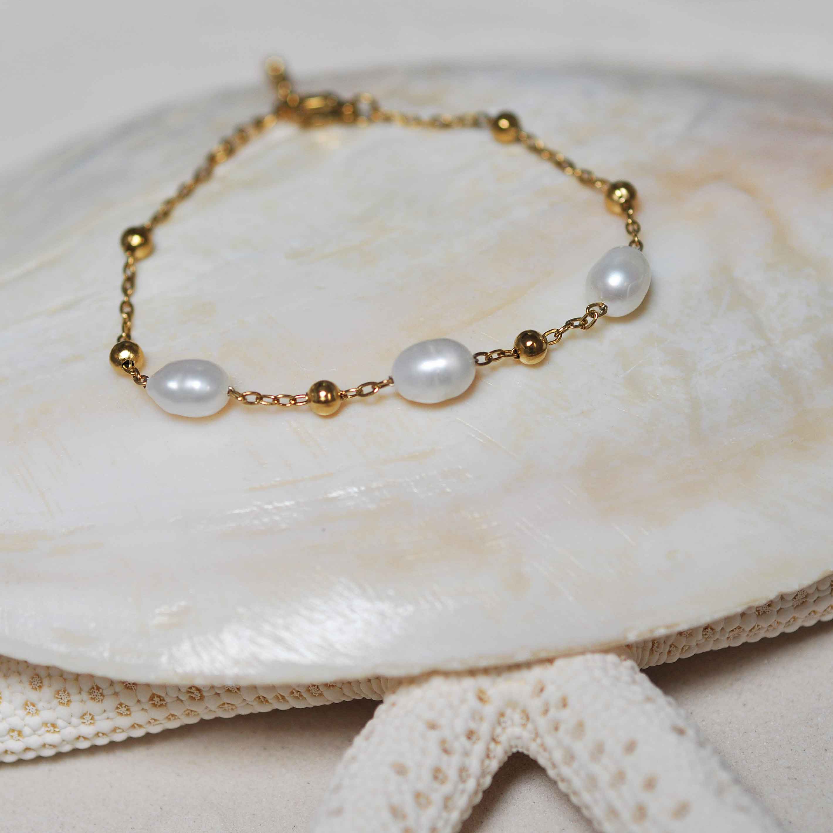 Wit zoetwater parel armband met goud edelstaal liggend op witte schelp | Parel armband Eline Goud