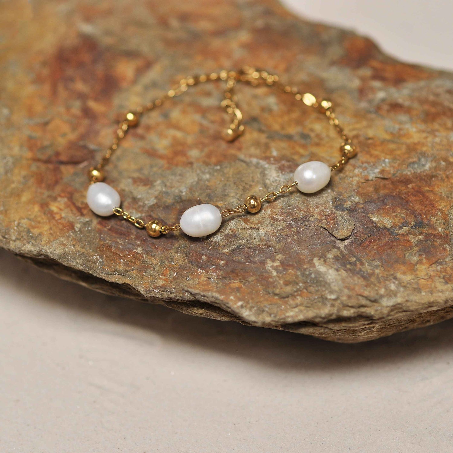 Wit zoetwater parel armband met goud edelstaal schuin liggend op steen | Parel armband Eline Goud