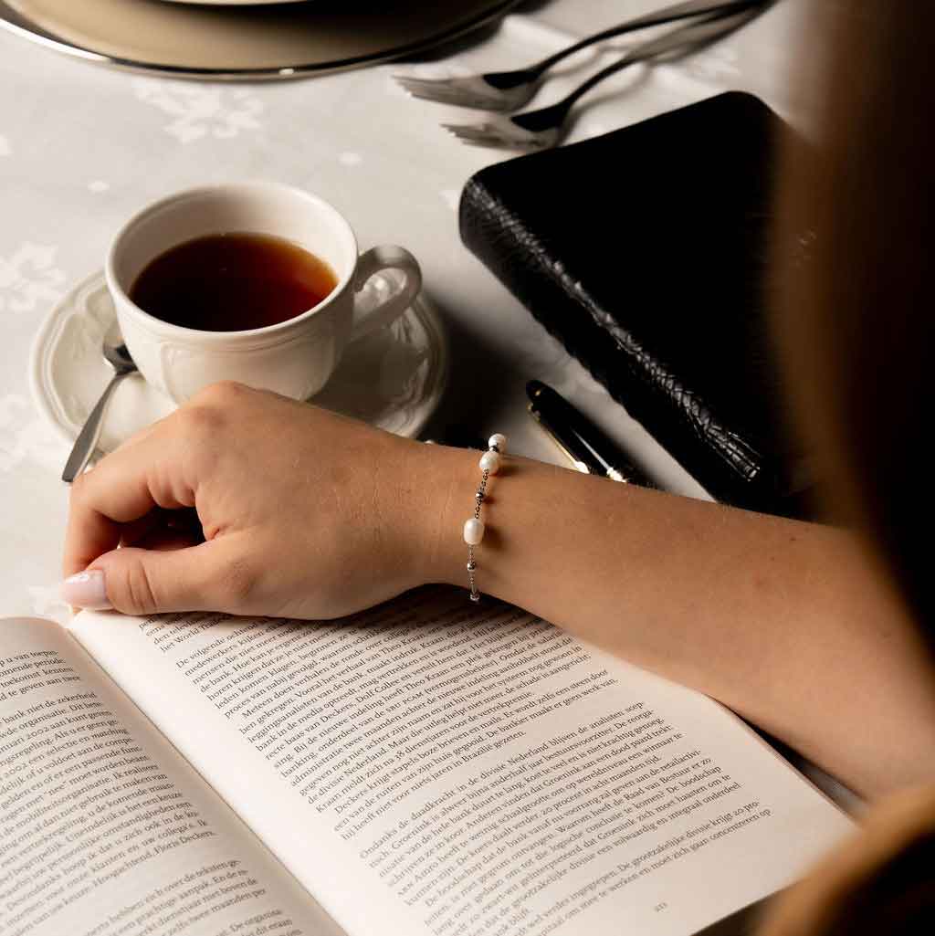 Wit zoetwater parel armband met zilver edelstaal gedragen door model die boek leest | Parel armband Eline Zilver