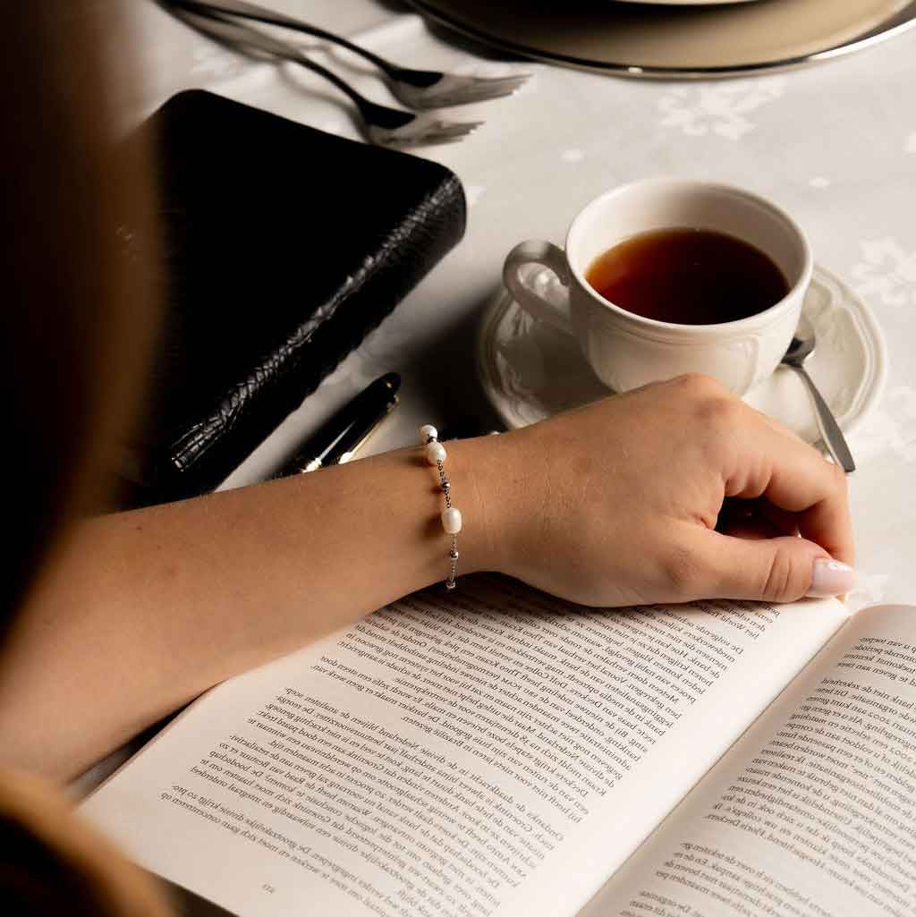 Wit zoetwater parel armband met zilver edelstaal gedragen door model die boek leest | Parel armband Eline Zilver