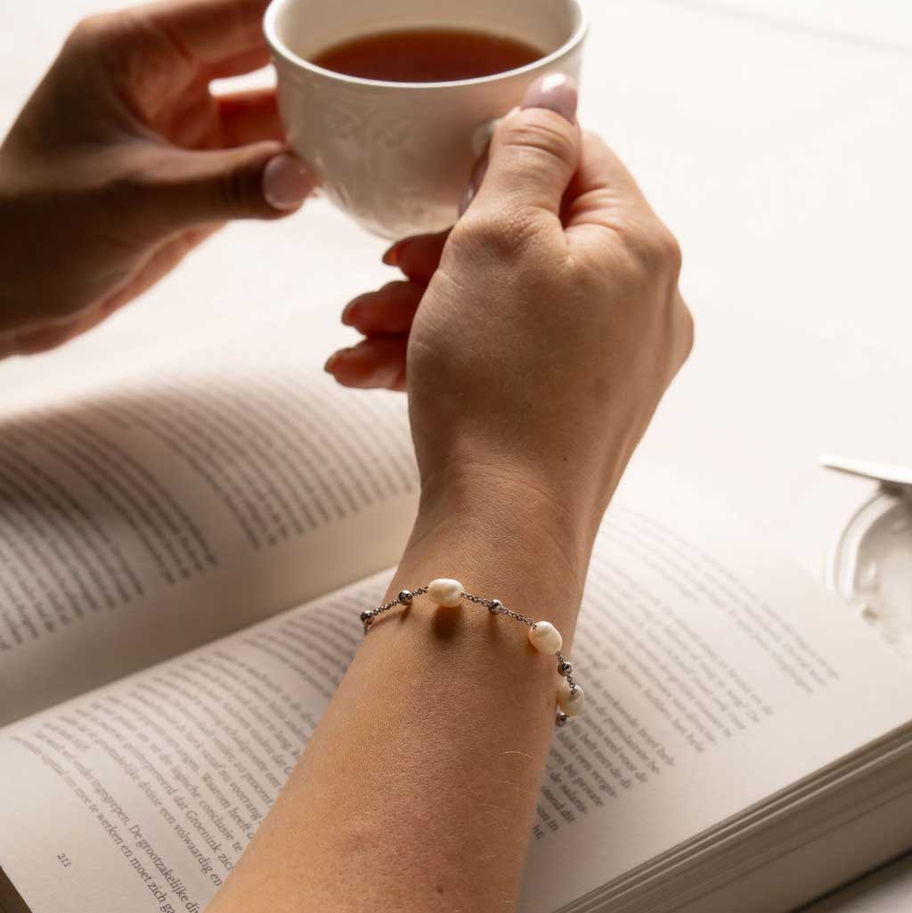 Wit zoetwater parel armband met zilver edelstaal gedragen door model die boek leest en thee drinkt | Parel armband Eline Zilver