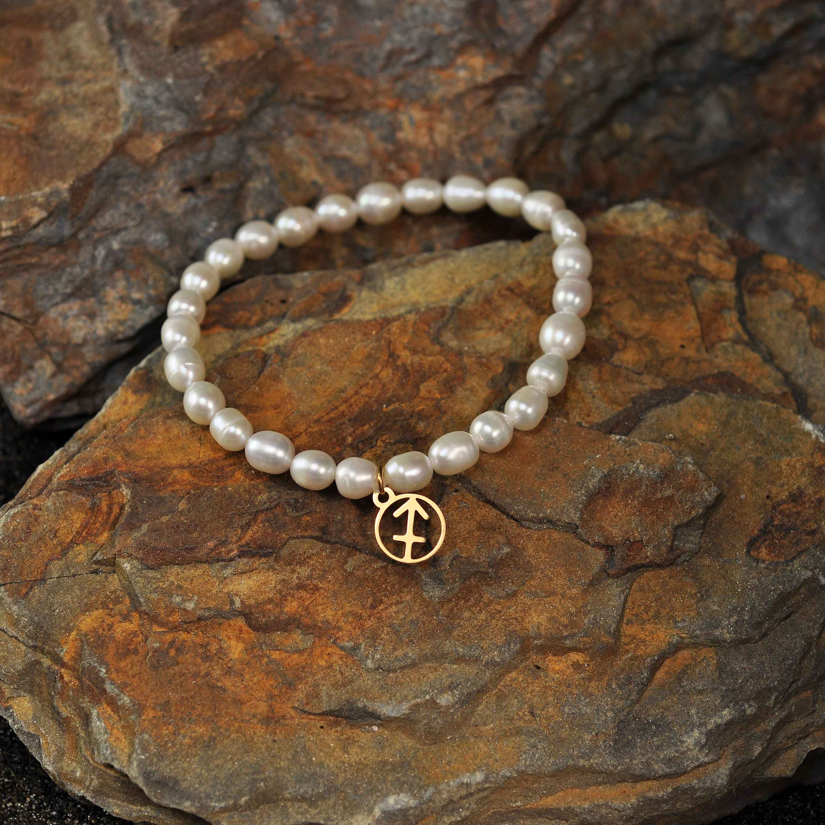 Wit zoetwater parel armband met gouden symbool sterrenbeeld boogschutter liggend op steen| Parel armband Gouden sterrenbeeld