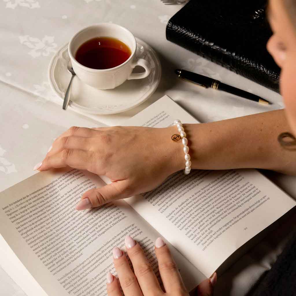 Wit zoetwater parel armband met gouden symbool sterrenbeeld boogschutter op model die boek leest | Parel armband Gouden sterrenbeeld Boogschutter
