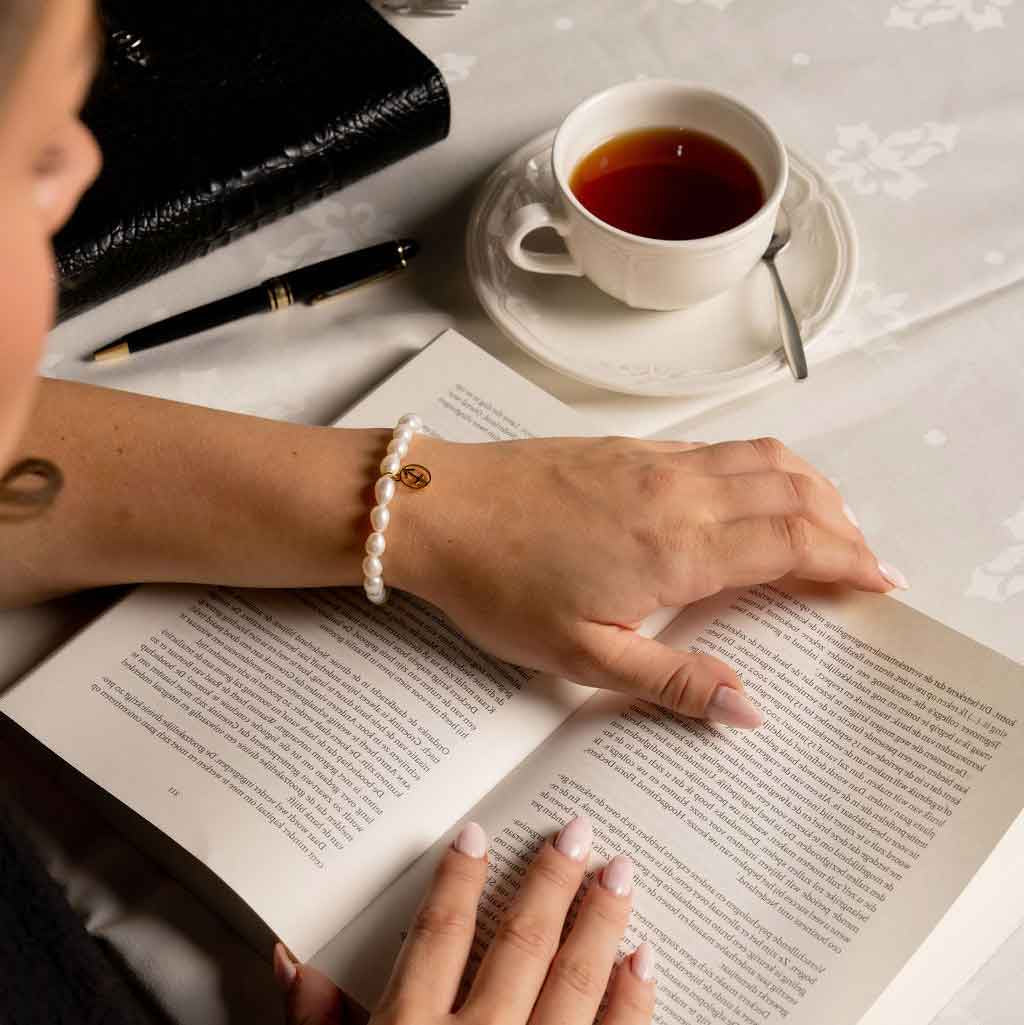 Wit zoetwater parel armband met gouden symbool sterrenbeeld boogschutter op model die boek leest | Parel armband Gouden sterrenbeeld Boogschutter