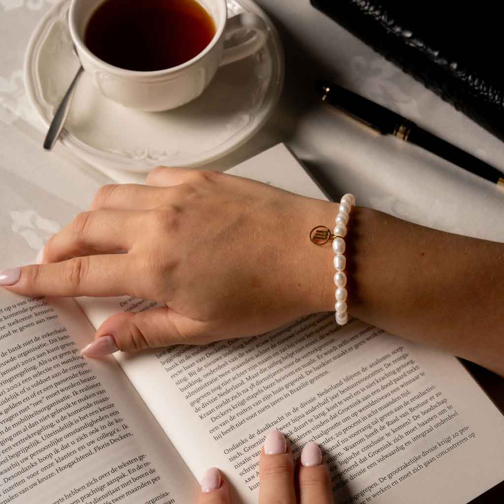 Wit zoetwater parel armband met symbool van sterrenbeeld schorpioen in edelstaal op model die boek leest | Gouden Sterrenbeeld Schorpioen