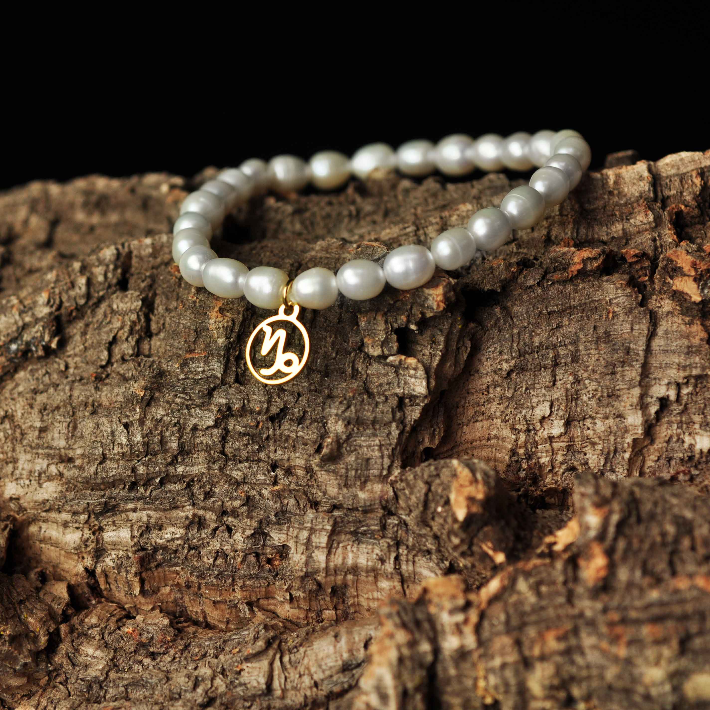Wit parel armband met gouden edelstalen symbool sterrenbeeld steenbok liggend op hout | Parel armband Gouden