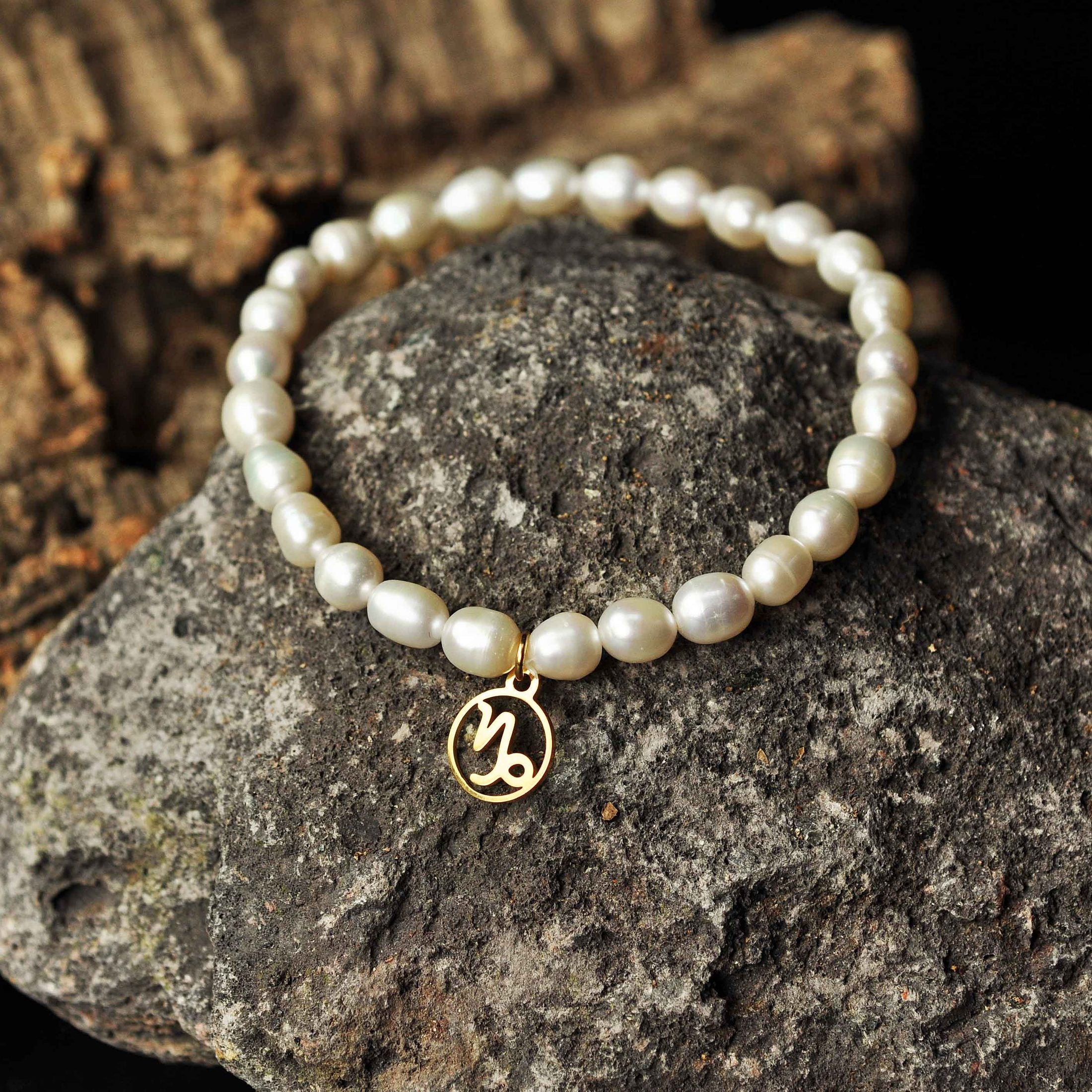 Wit parel armband met gouden edelstalen symbool sterrenbeeld steenbok liggend op zwarte steen | Parel armband Gouden