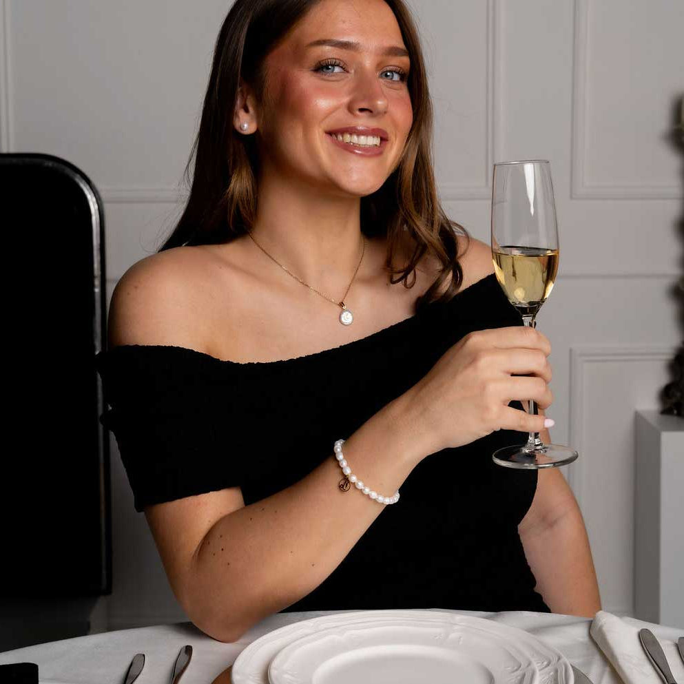 Wit parel armband met gouden edelstalen symbool sterrenbeeld steenbok op model aan tafel | Parel armband Gouden Sterrenbeeld Steenbok