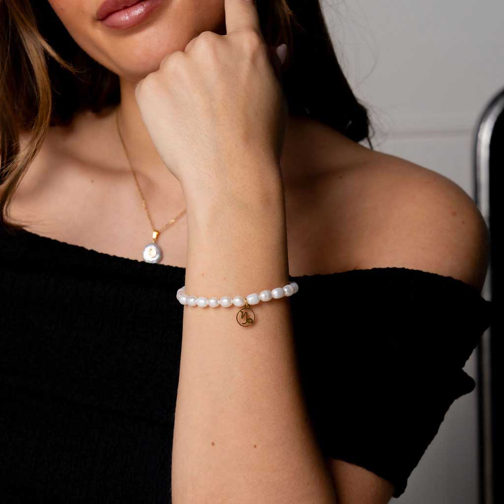 Wit parel armband met gouden edelstalen symbool sterrenbeeld steenbok op model detail | Parel armband Gouden Sterrenbeeld Steenbok