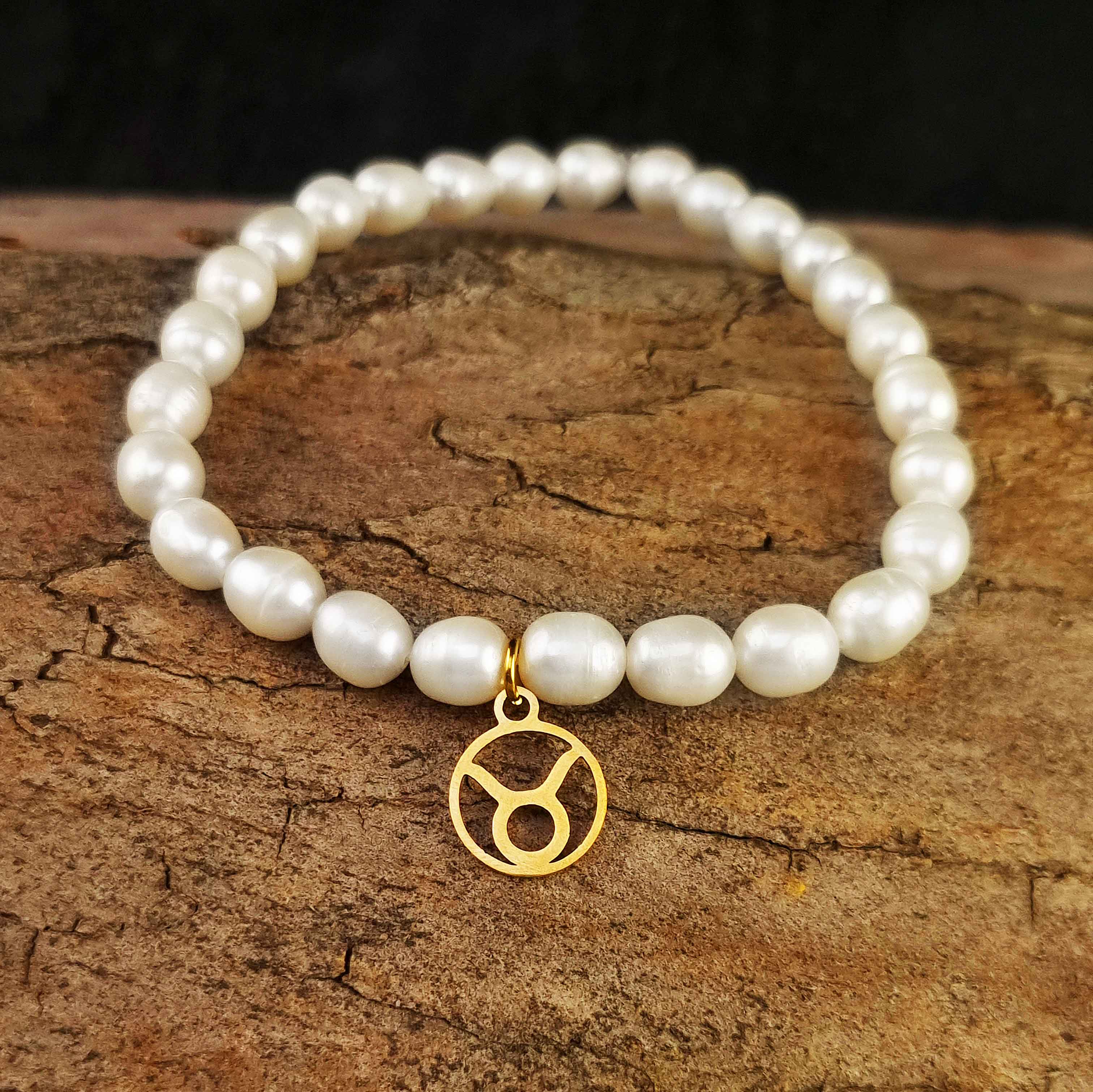 Wit zoetwater parel armband met goud edelstalen bedeltje van sterrenbeeld Stier liggend op hout | Gouden Sterrenbeeld Stier