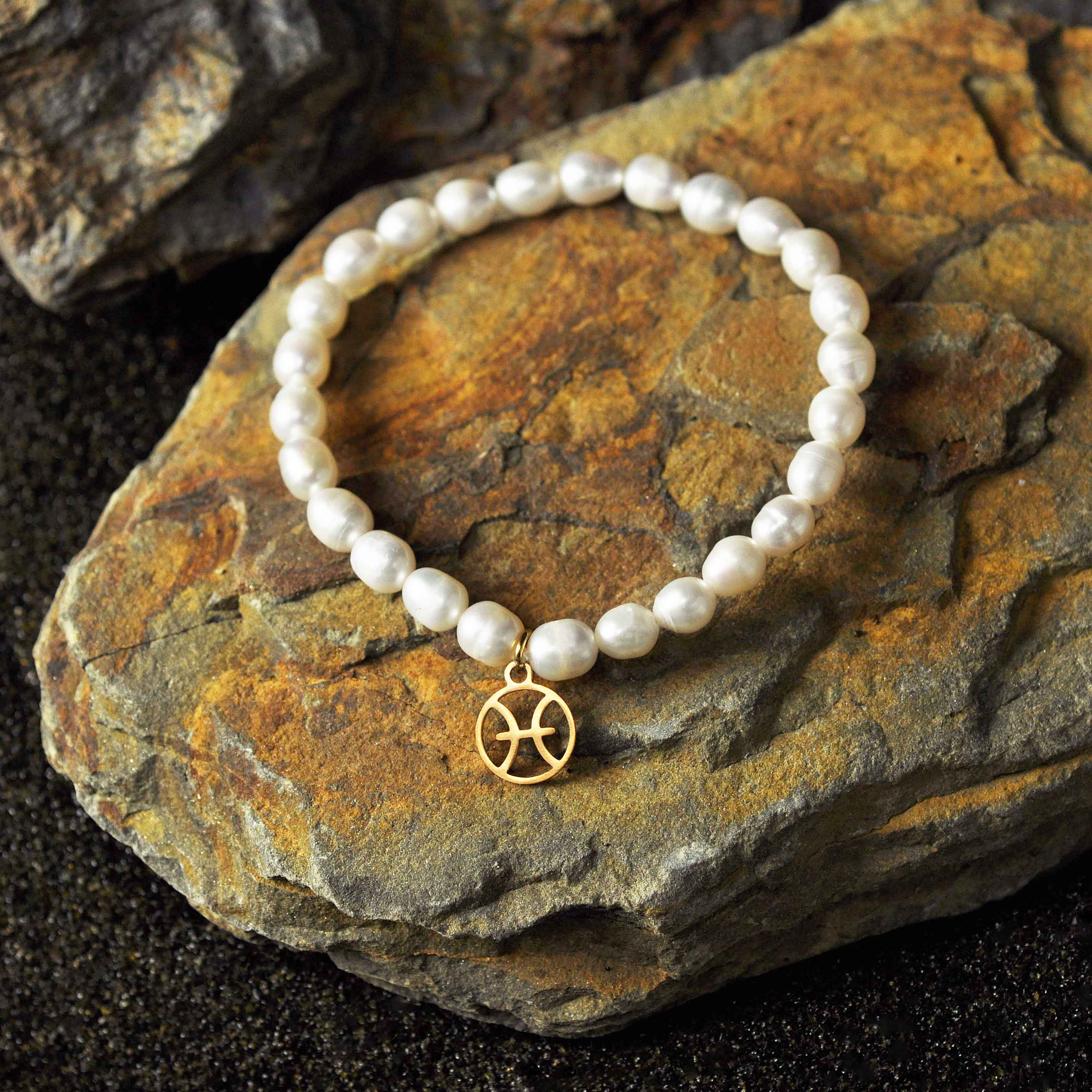Wit zoetwater parel armband met goud edelstalen symbool sterrenbeeld Vissen liggend op steen | Parel armband Gouden Sterrenbeeld Vissen