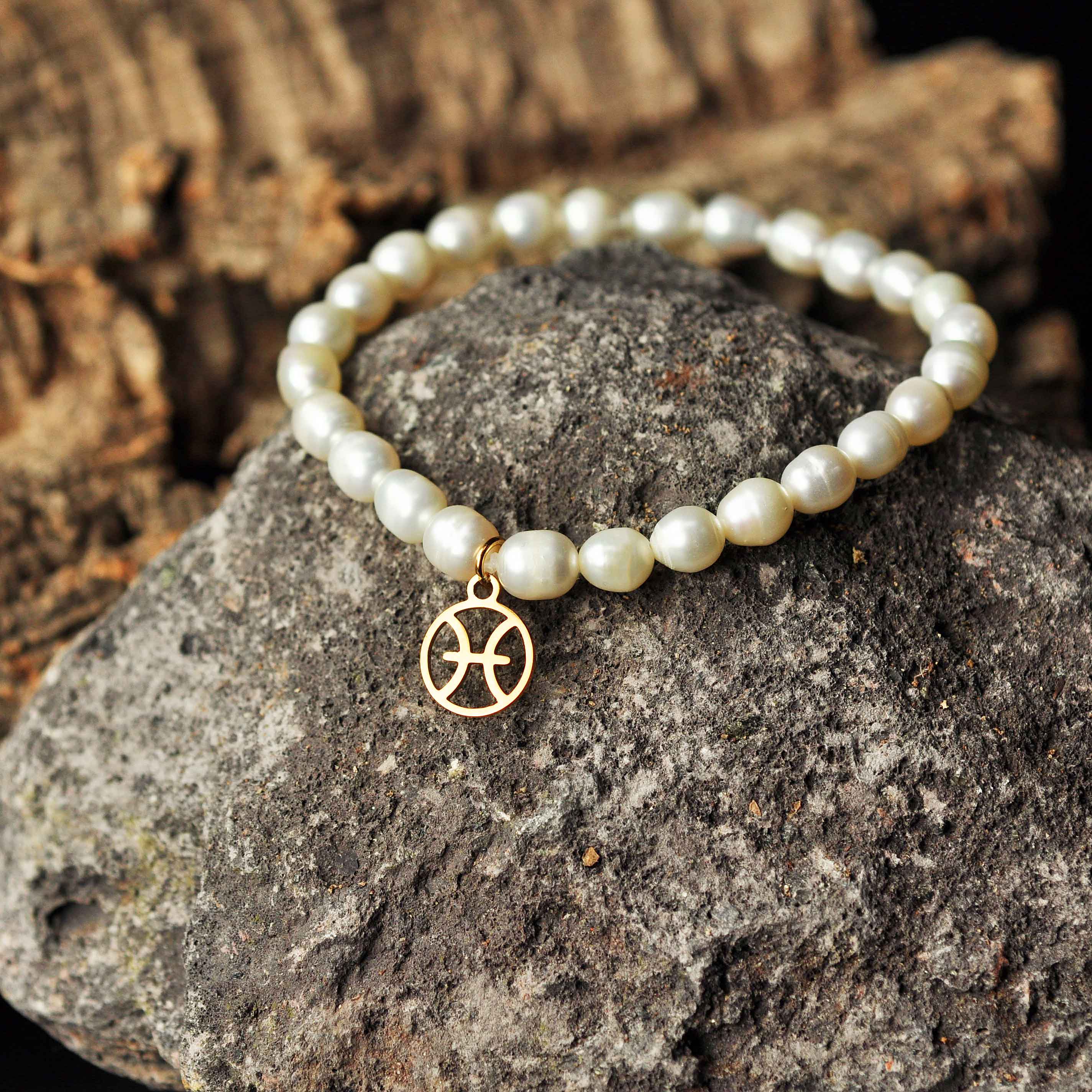 Wit zoetwater parel armband met goud edelstalen symbool sterrenbeeld Vissen liggend op zwarte steen | Parel armband Gouden Sterrenbeeld Vissen
