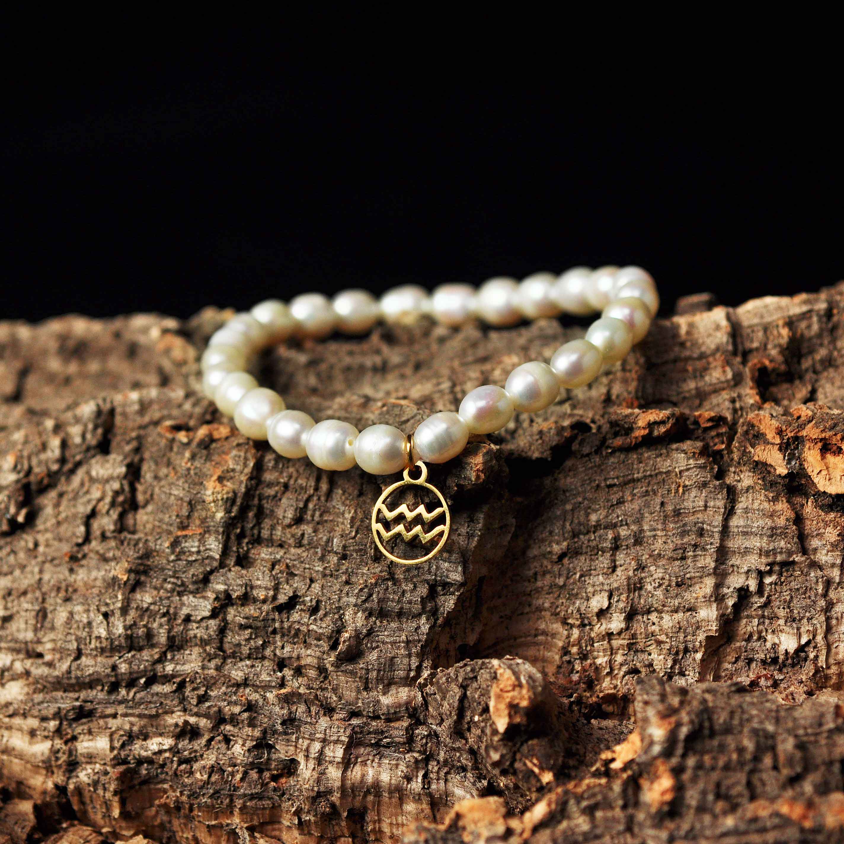 Wit zoetwater parel armband met goud edelstalen symbool van sterrenbeeld Waterman liggend op schors | Parel armband Gouden sterrenbeeld Waterman
