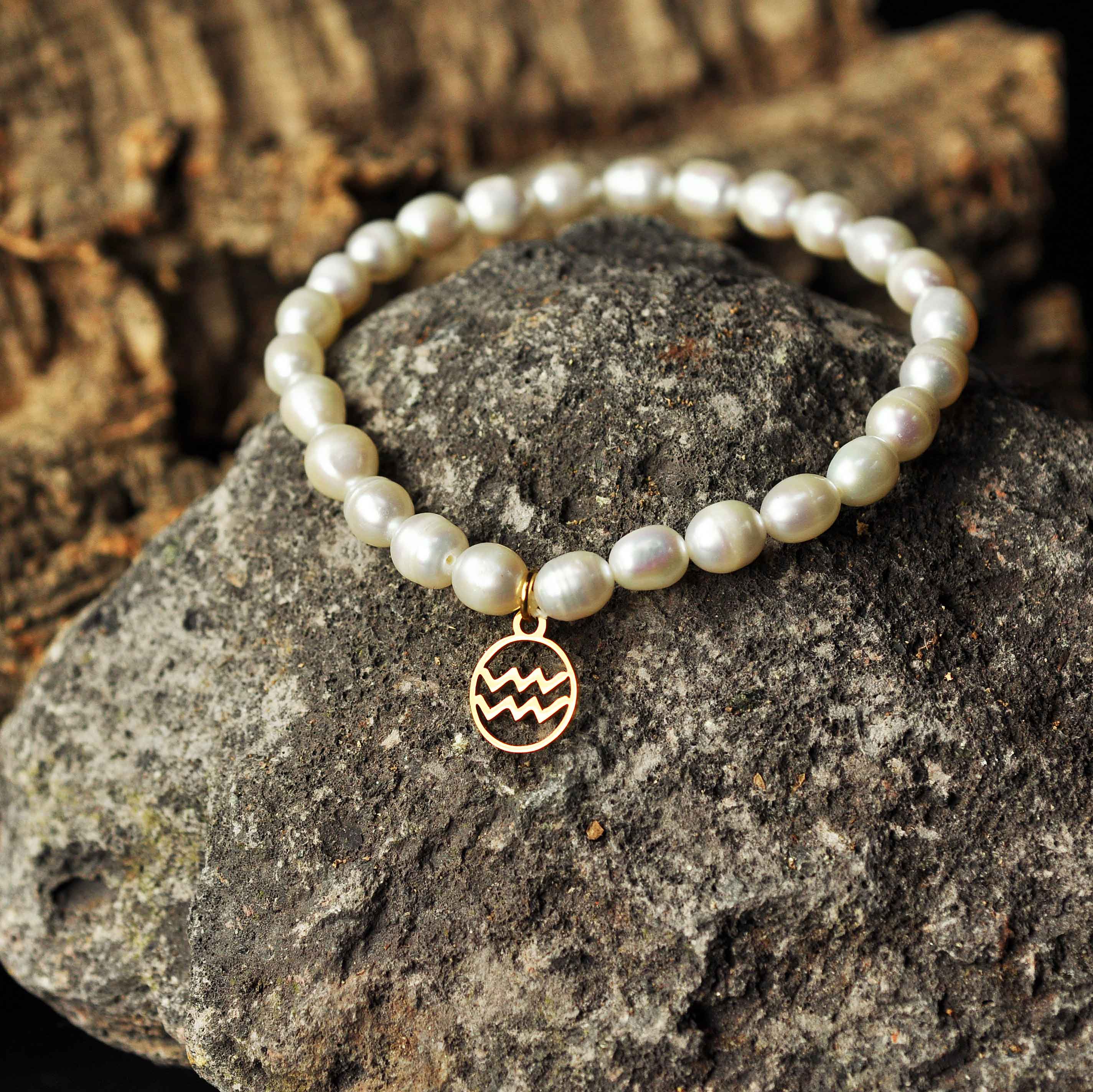 Wit zoetwater parel armband met goud edelstalen symbool van sterrenbeeld Waterman liggend op zwarte steen| Parel armband Gouden sterrenbeeld Waterman