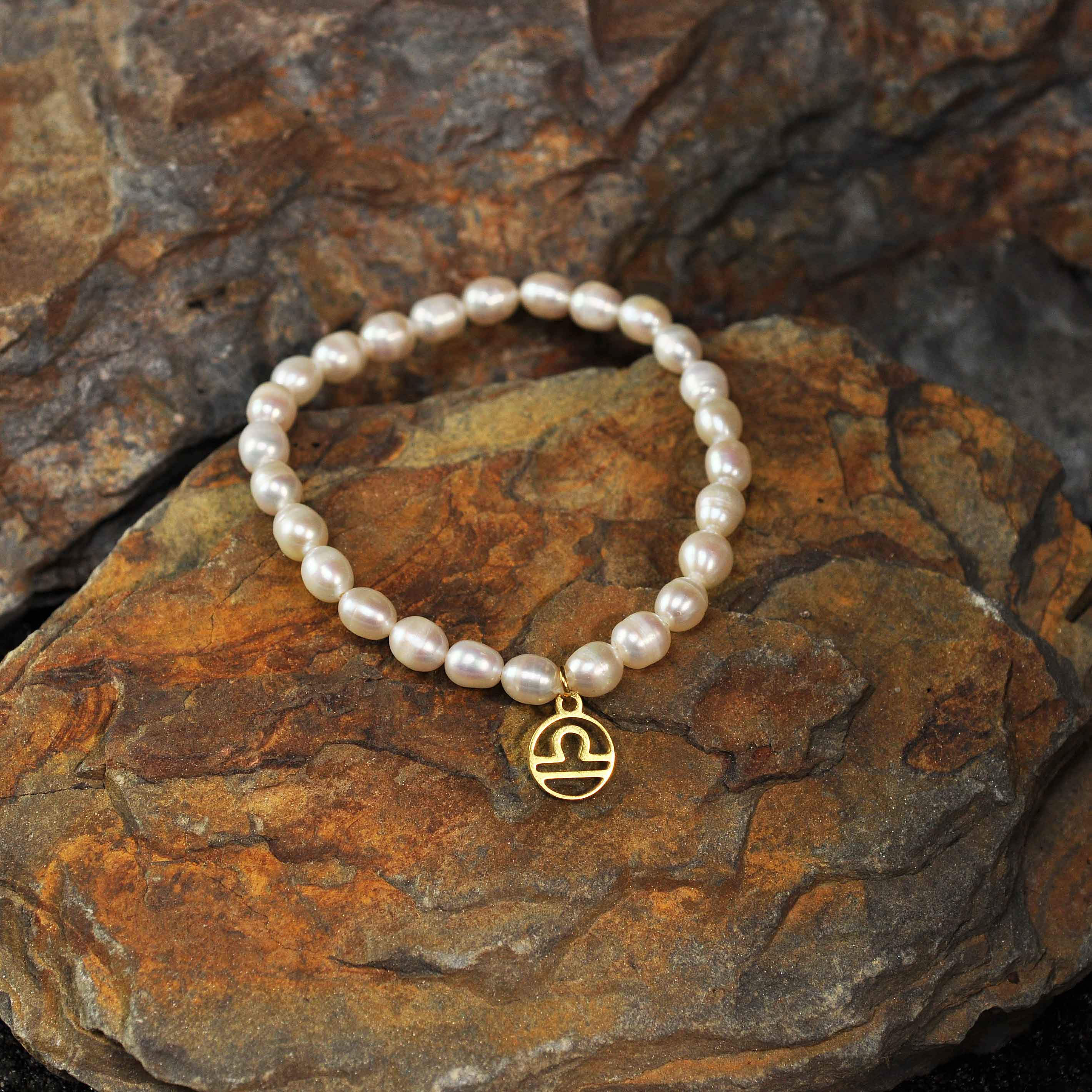 Wit zoetwater parel armband met goud edelstalen symbool van sterrenbeeld Weegschaal liggend op steen | Armband Gouden Sterrenbeeld Weegschaal
