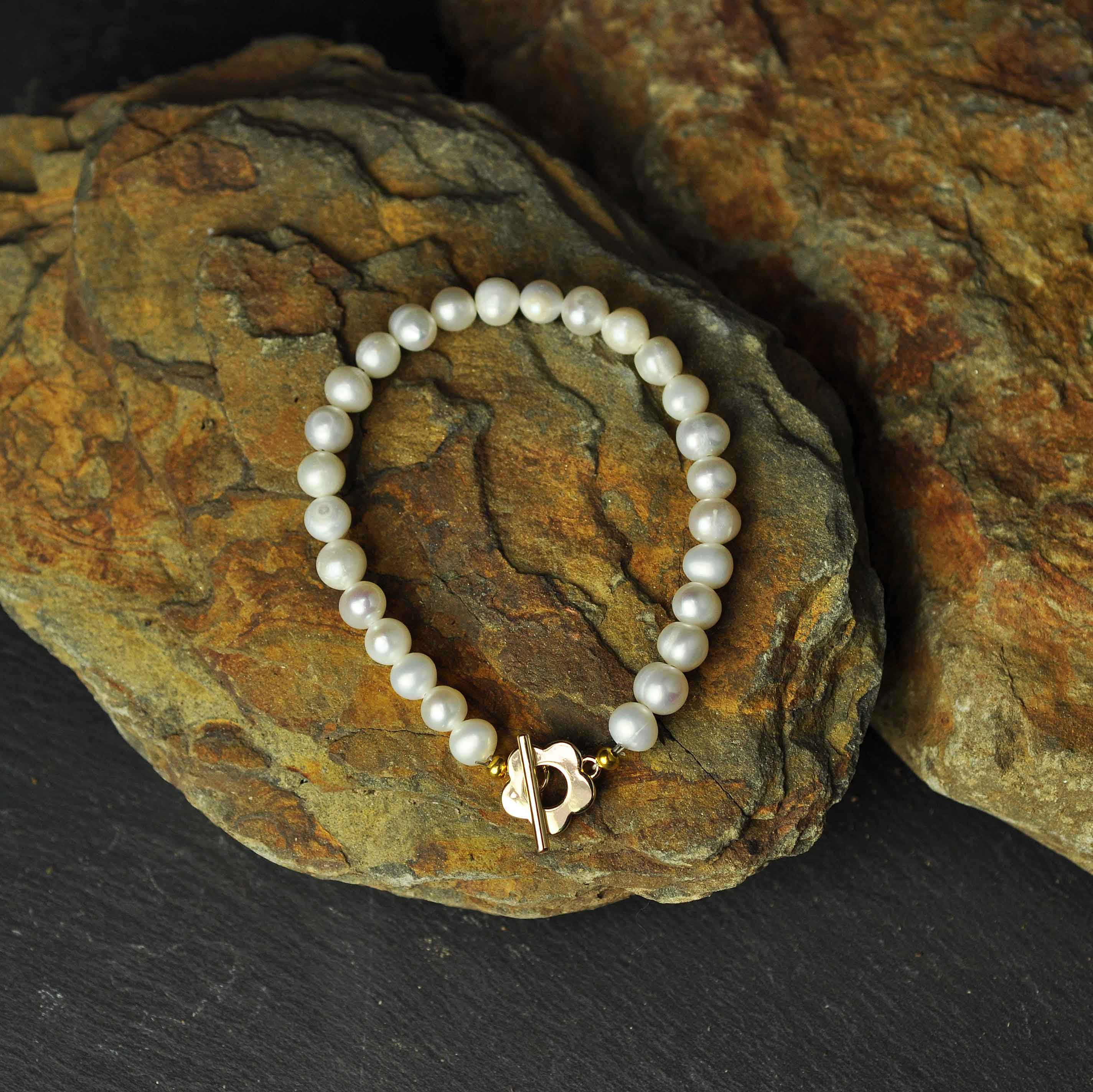 Wit zoetwater parel armband met gouden bloem slotje liggend op oranje steen | Pearl Golden Flower