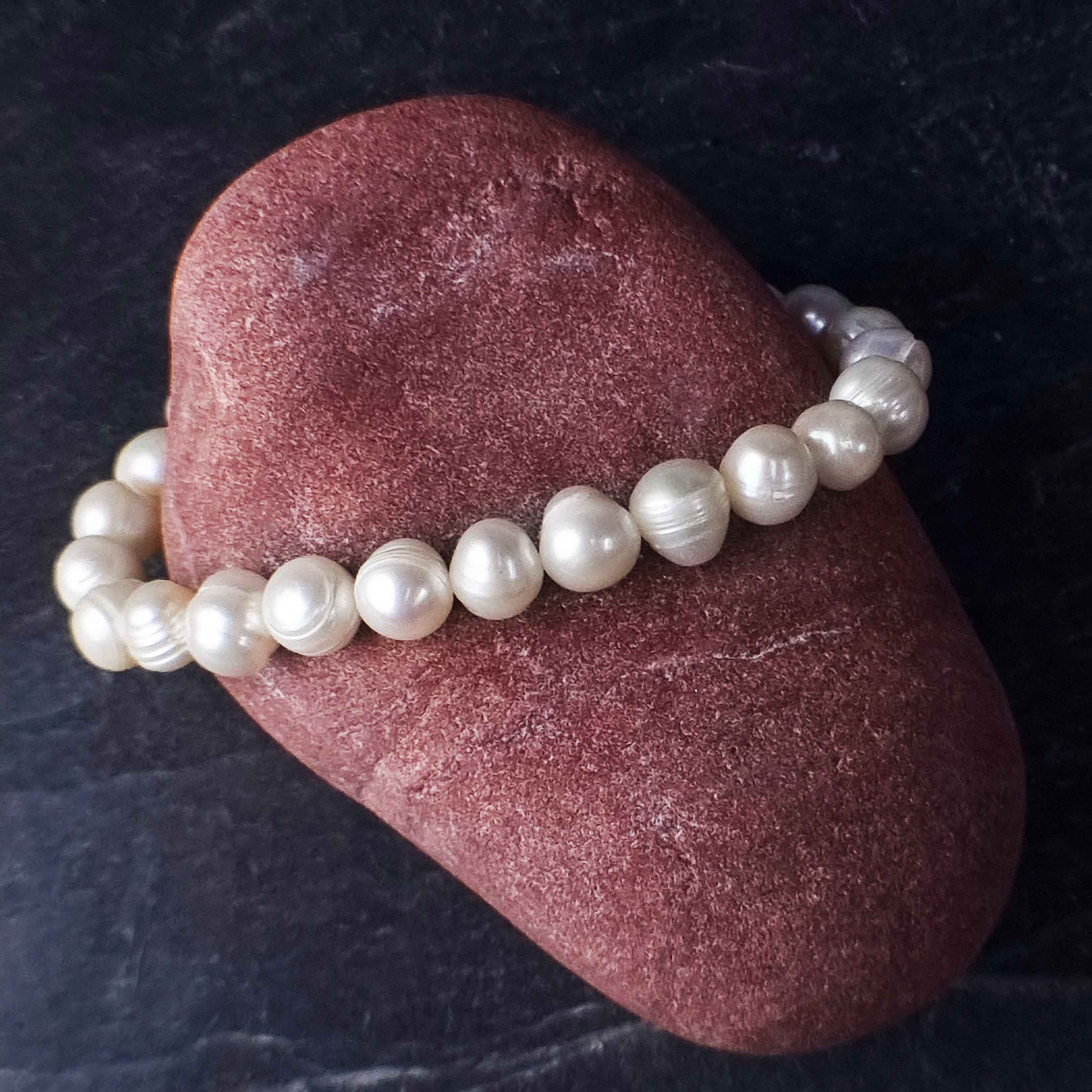 Wit elastisch zoetwater parel armband liggend op rode steen | Round White