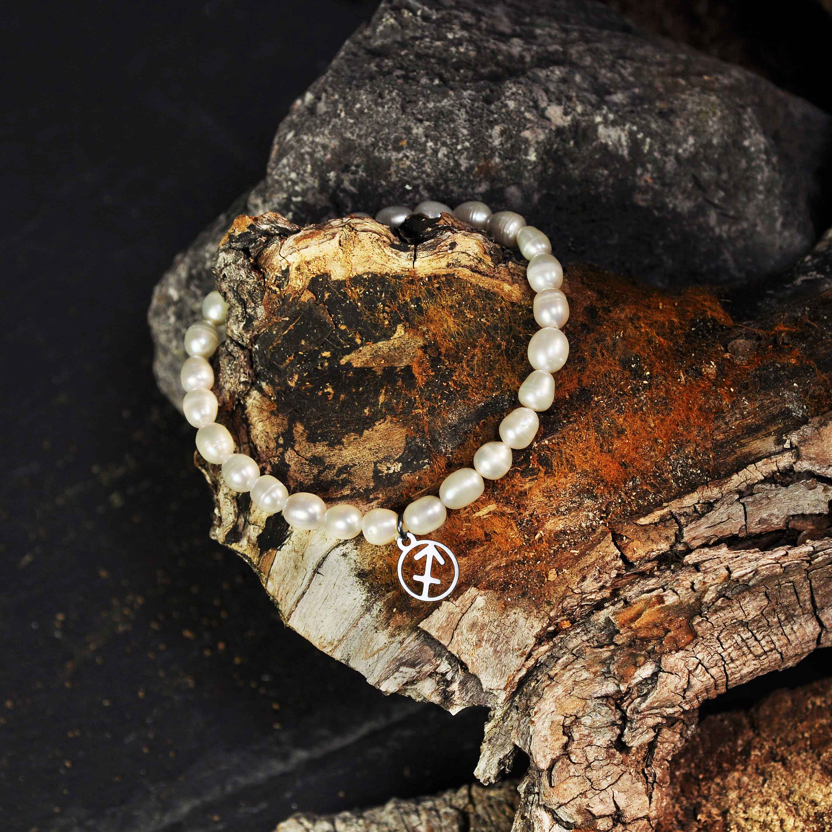 Wit zoetwater parel armband met zilveren symbool sterrenbeeld boogschutter liggend op hout | Parel Armband Zilveren Sterrenbeeld Boogschutter